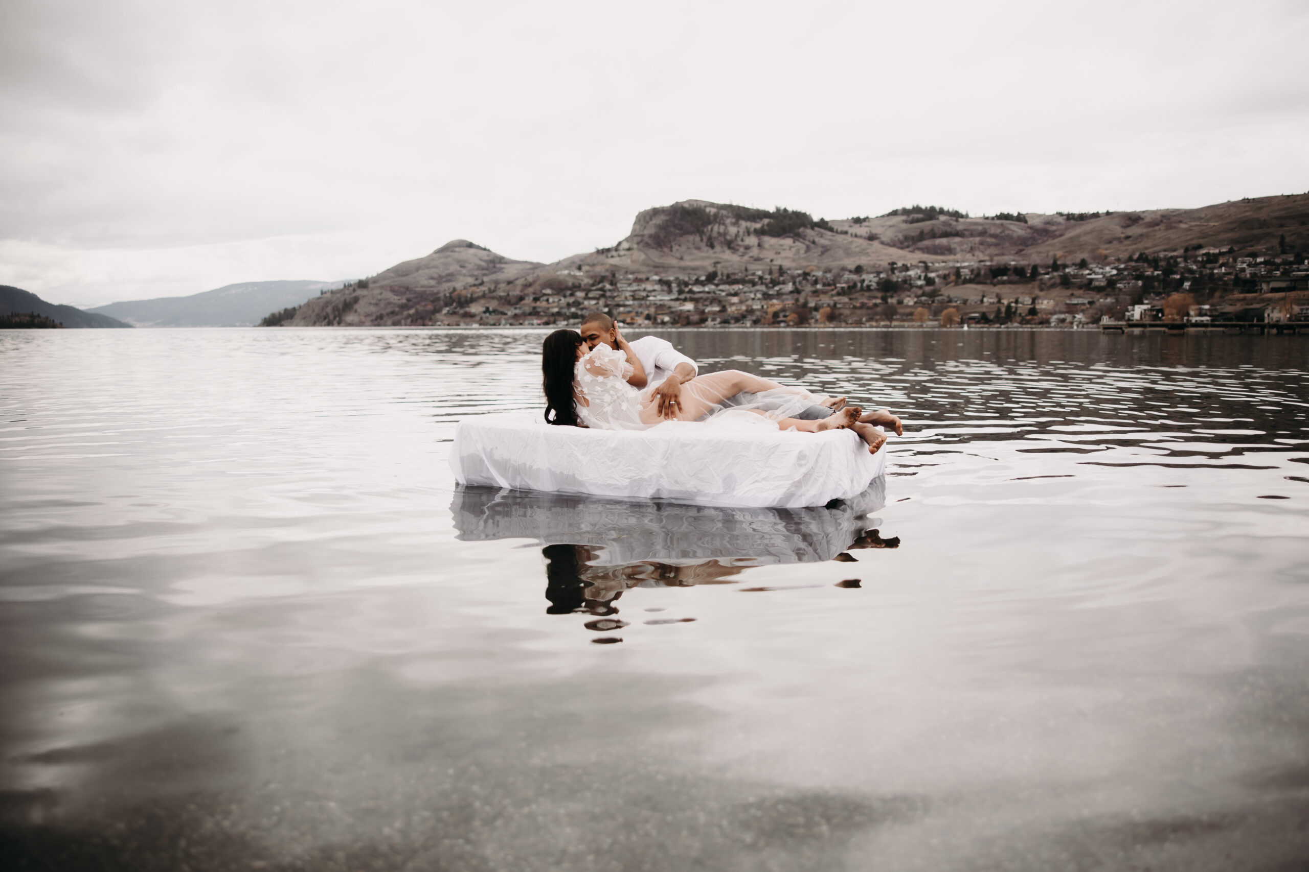 Unique engagement photo ideas come to life as the couple enjoys an intimate moment on a floating air mattress, surrounded by the peaceful waters and mountain views.