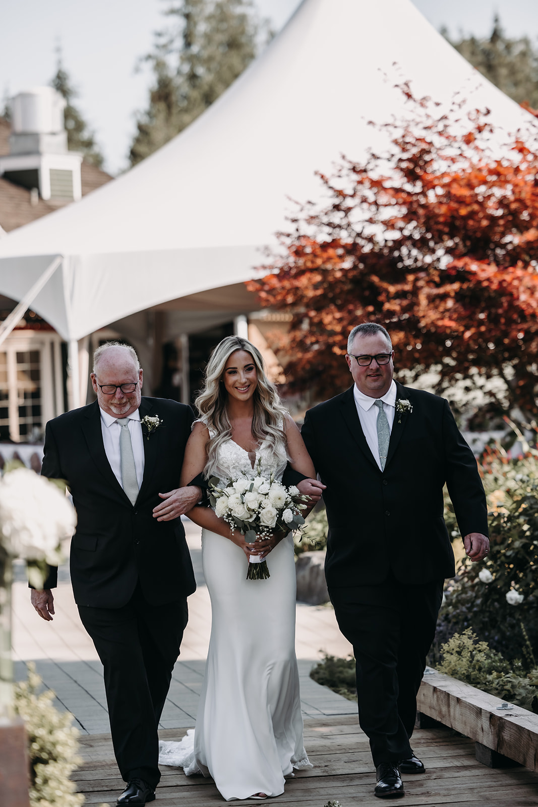 Bride walking down the aisle with her father and adopted father at her Redwoods Golf Course wedding, surrounded by a beautiful outdoor ceremony.