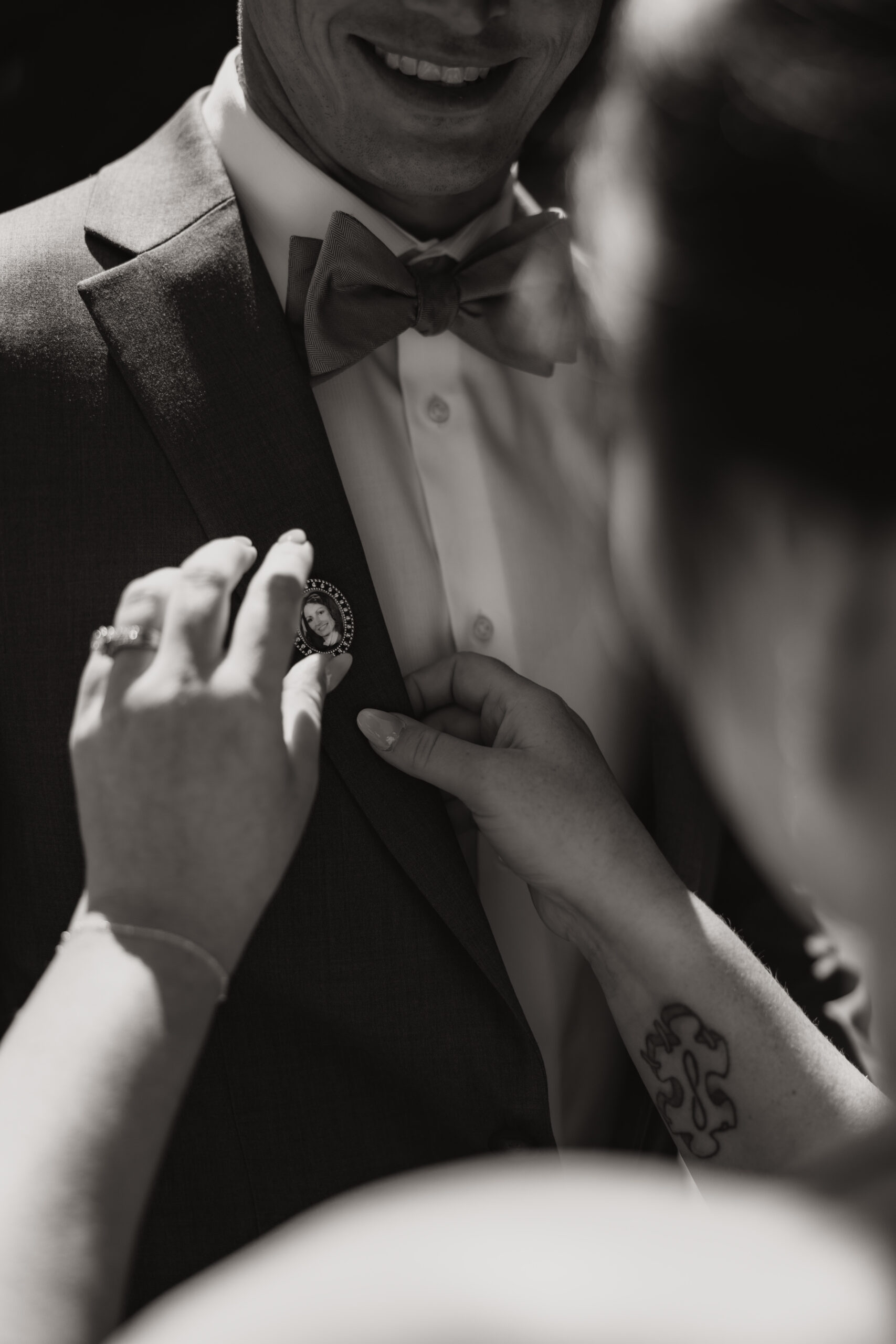 A close-up of a groom’s suit as the bride fastens a sentimental pin with a photo of a loved one. This emotional moment at the Redwoods Golf Course wedding highlights the love and personal touches.