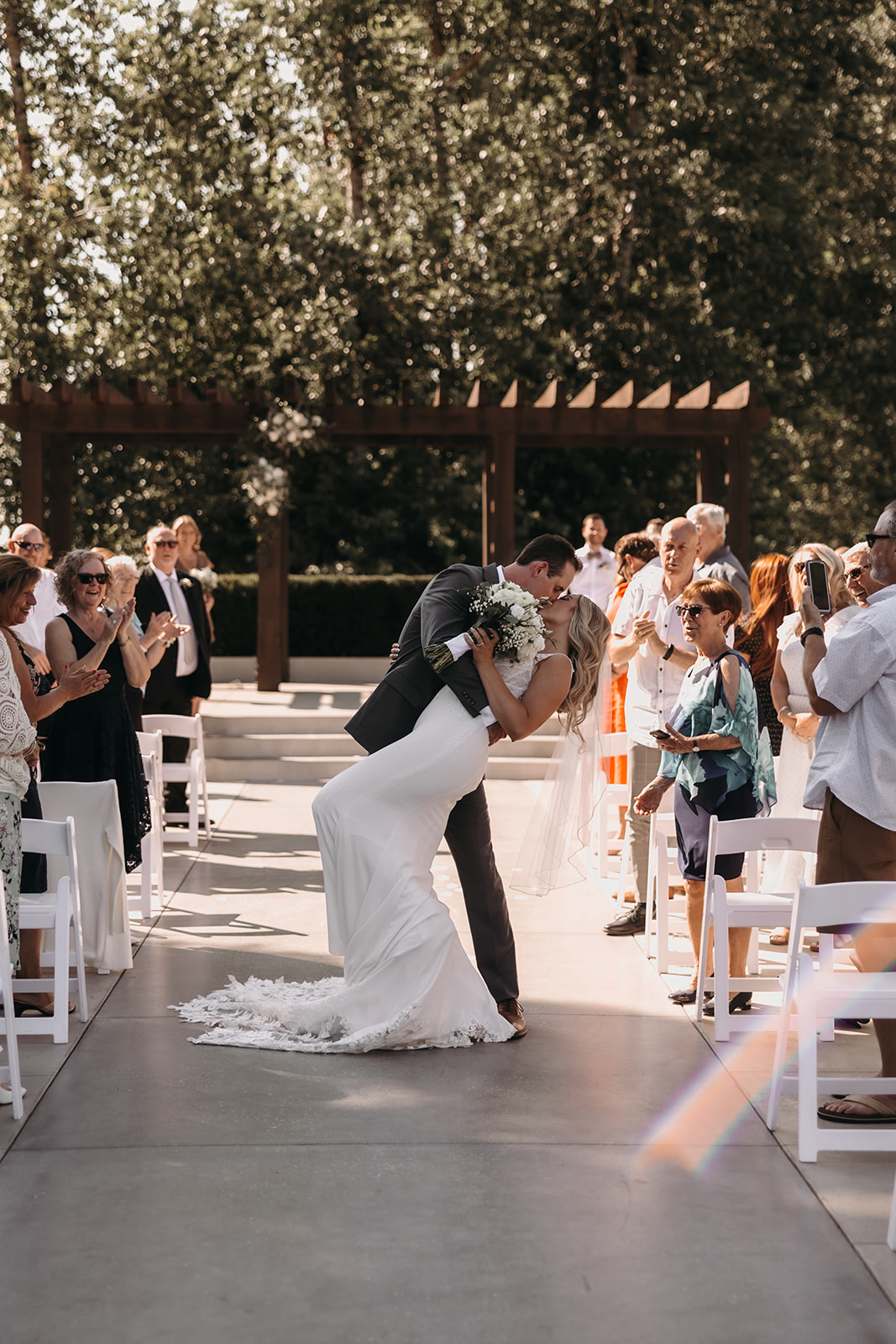 A newlywed couple sharing a passionate kiss after their ceremony at the Redwoods Golf Course wedding venue, surrounded by cheering guests.