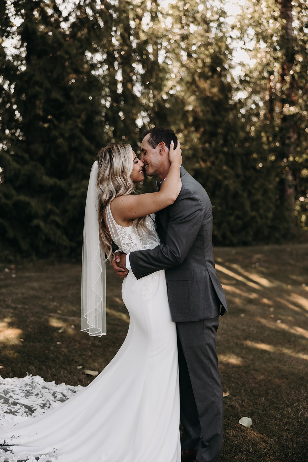 The bride gazing lovingly at her groom as they embrace on a grassy lawn, enjoying a quiet moment after their wedding ceremony at Redwoods Golf Course.