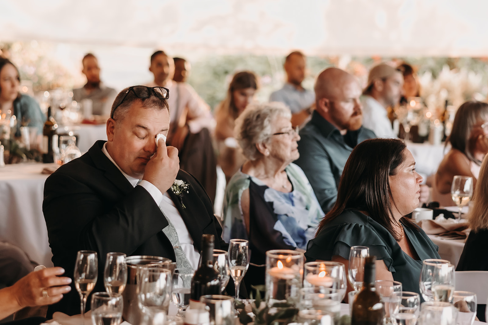 A guest wiping away a tear during the wedding reception at a Redwoods Golf Course Wedding, with guests enjoying their time in the background.