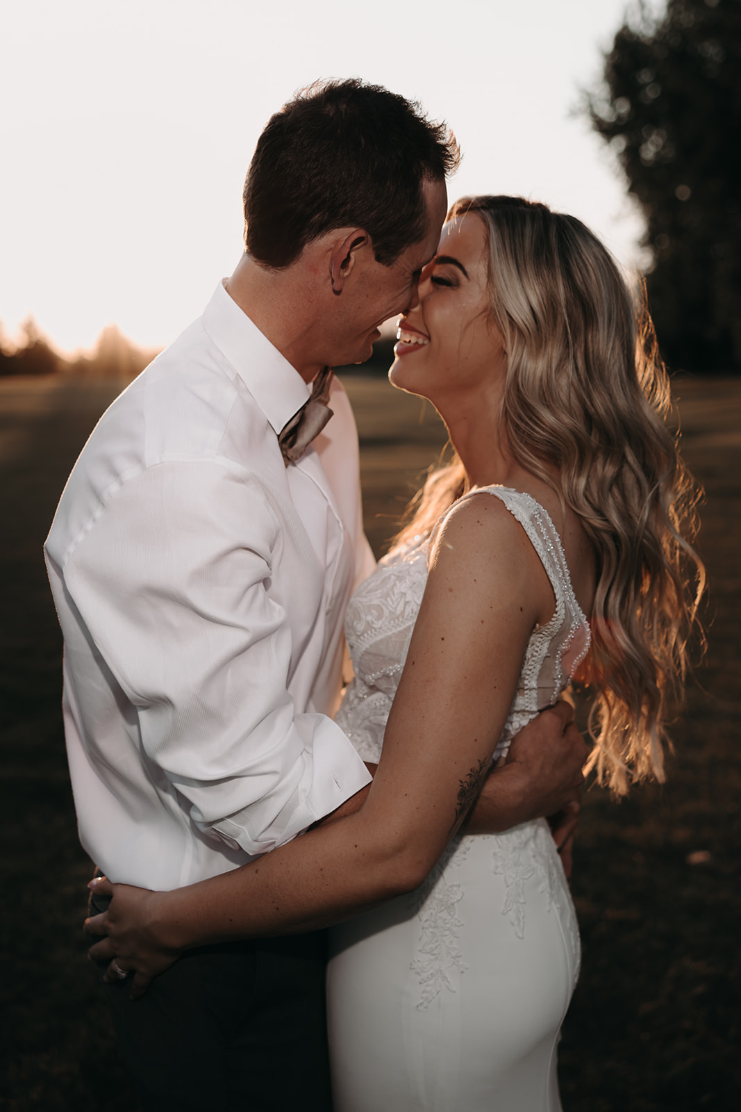 A sunset portrait of a couple at their Redwoods Golf Course wedding, the bride in a fitted gown with intricate lace details, gazing lovingly at her husband as they share a kiss.