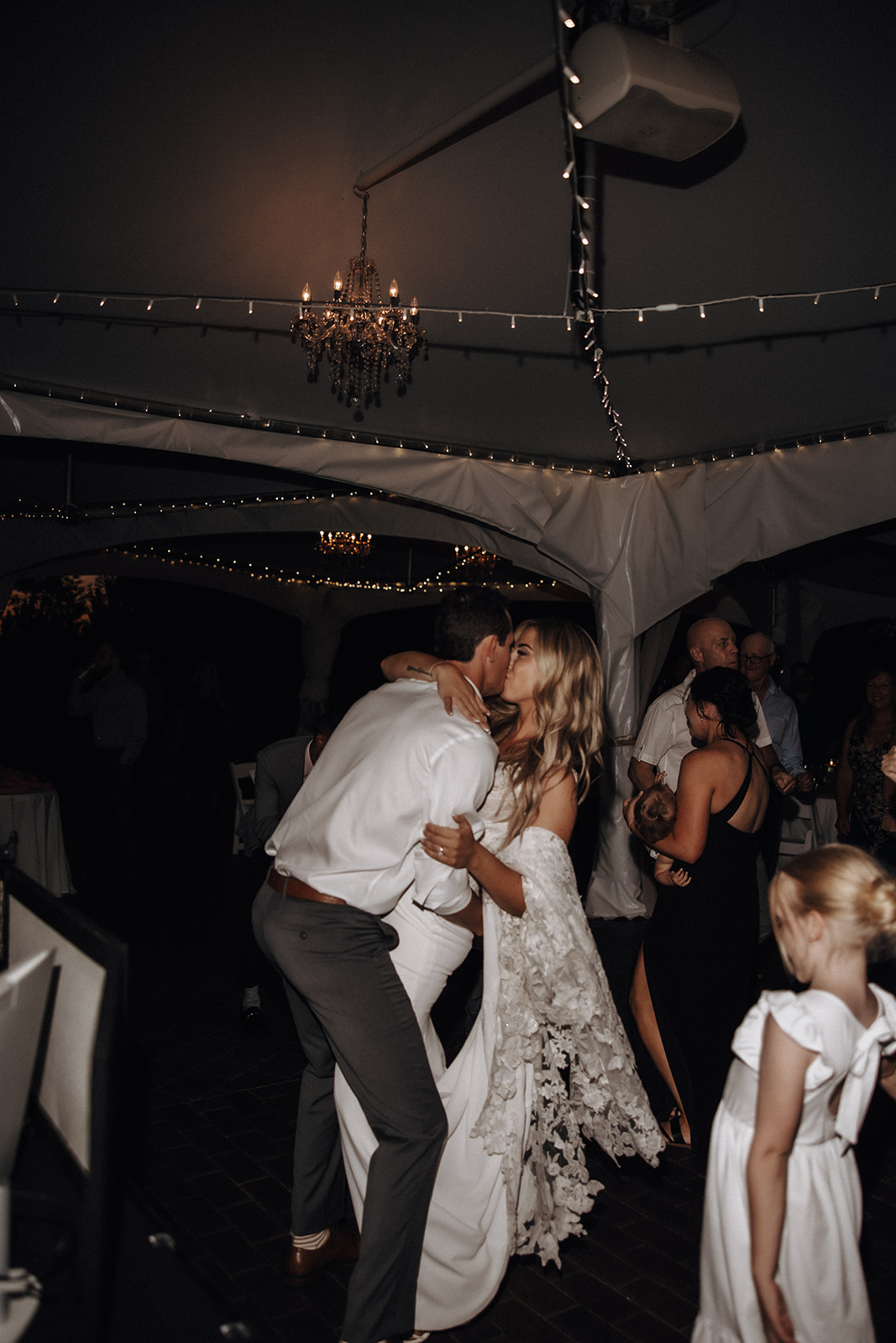 The couple dances with joy under twinkling lights at their reception following their Redwoods Golf Course wedding. Surrounded by friends and family, they share a loving moment while others enjoy the lively celebration.