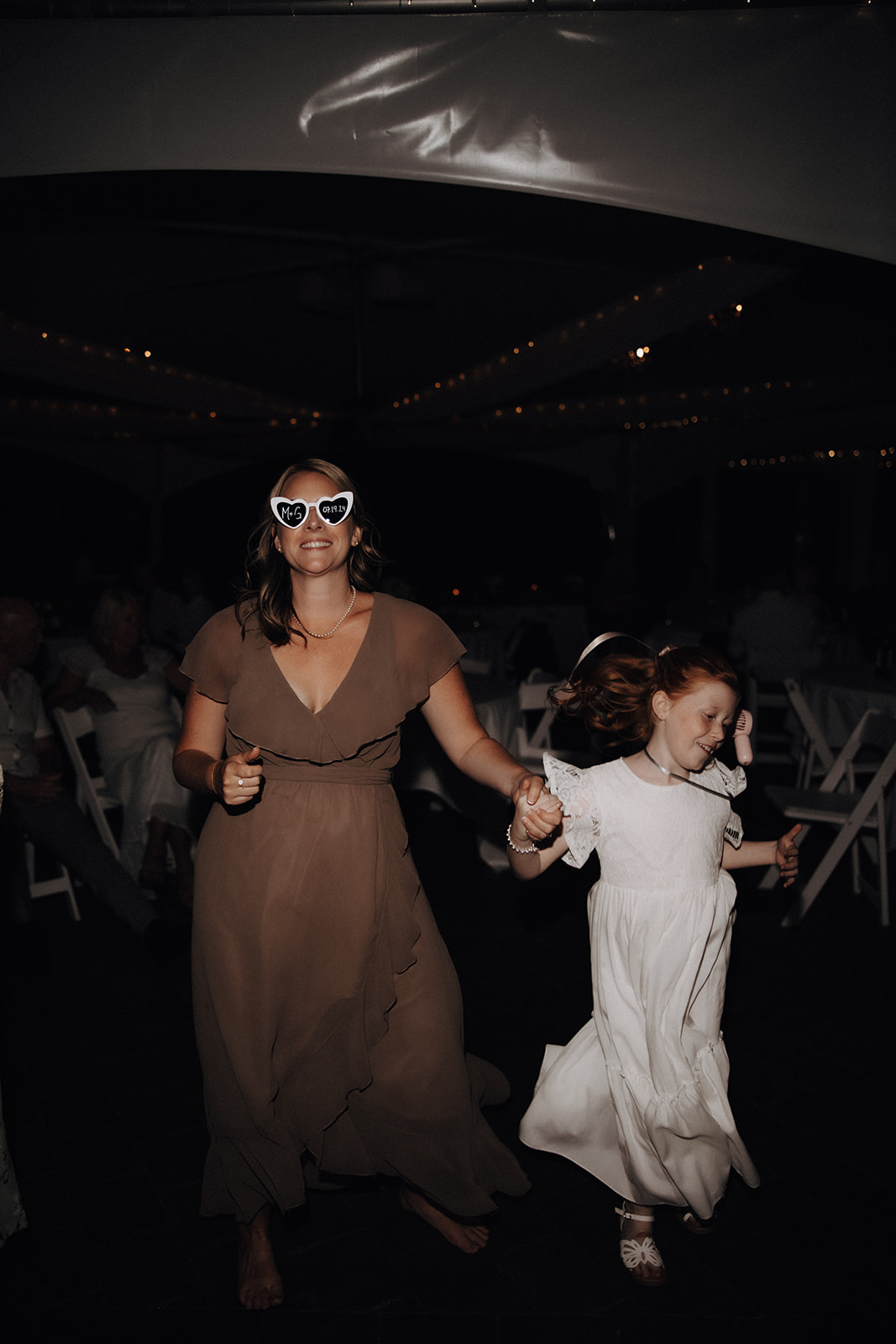 A mother and daughter dance together at a wedding reception at the Redwoods Golf Course Wedding, both wearing heart-shaped glasses while guests look on in the background.