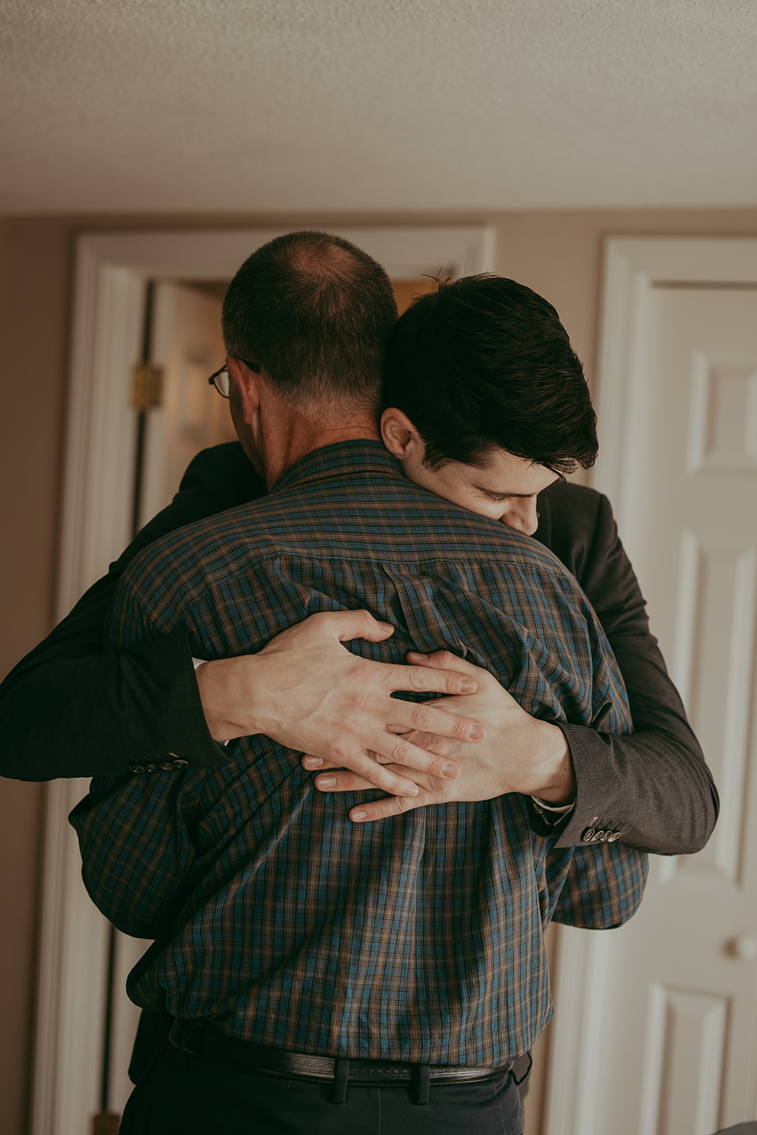 Groom and his father sharing an emotional hug before the wedding ceremony, a beautiful moment from their destination wedding in Maine.