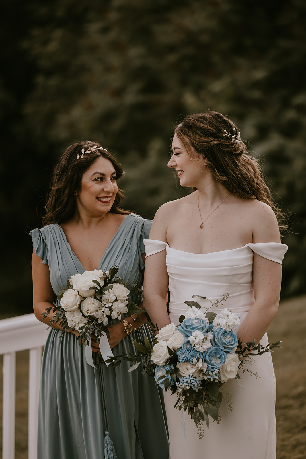 The bride and one of her bridesmaids share a joyful moment together, smiling and holding their beautiful floral arrangements during their destination wedding in Maine.