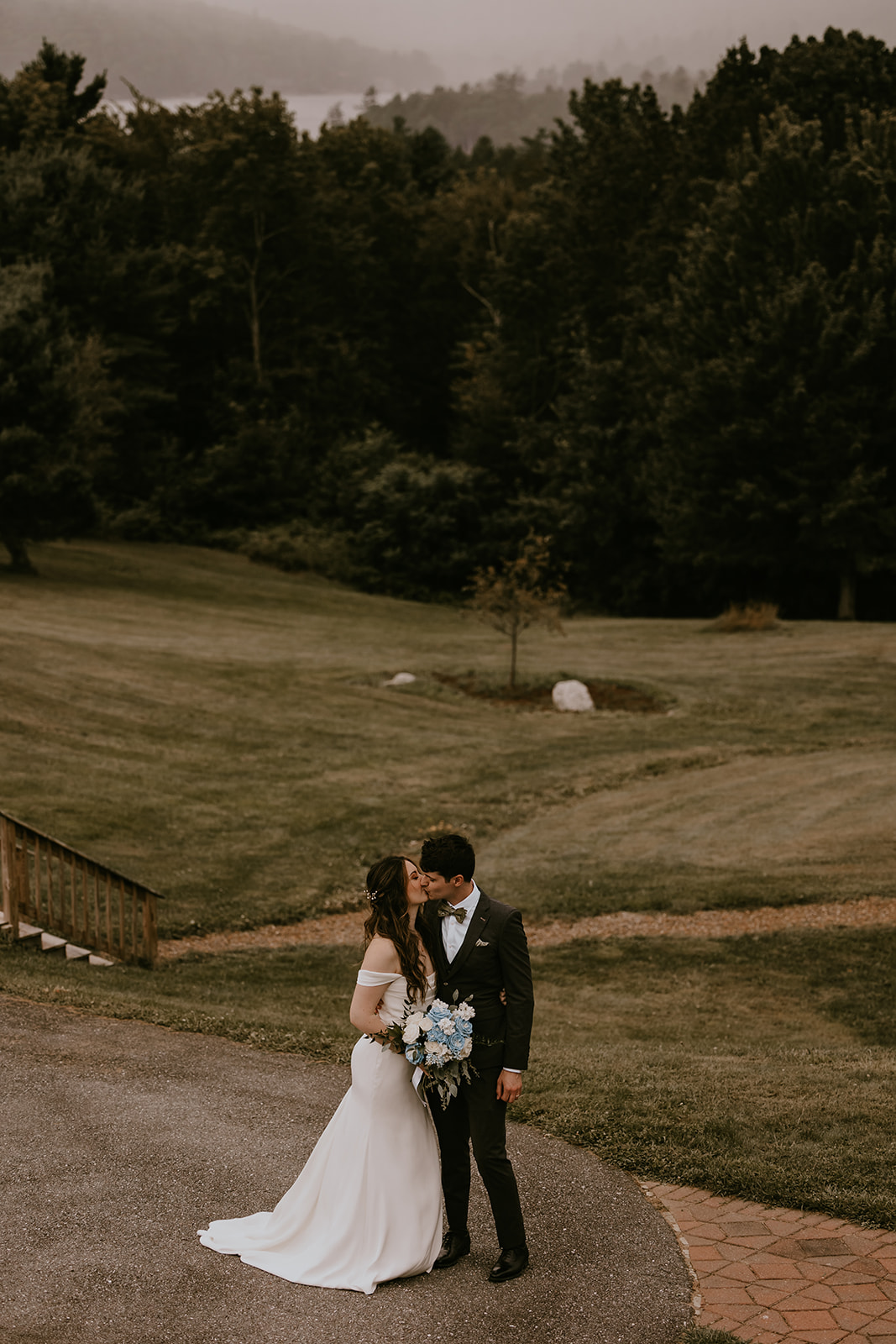 A romantic kiss between the couple during their destination wedding in Maine at the Lucerne Inn, Dedham, surrounded by the lush greenery of the Maine countryside.