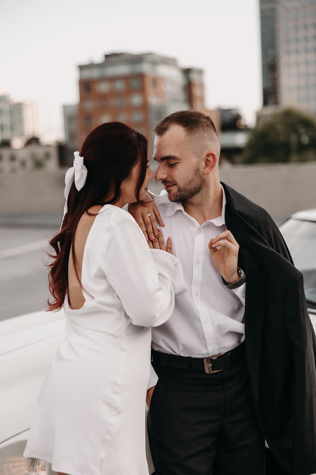 Close-up of a couple smiling and sharing a quiet moment during their city engagement photos on a Vancouver rooftop, with the city skyline behind them.