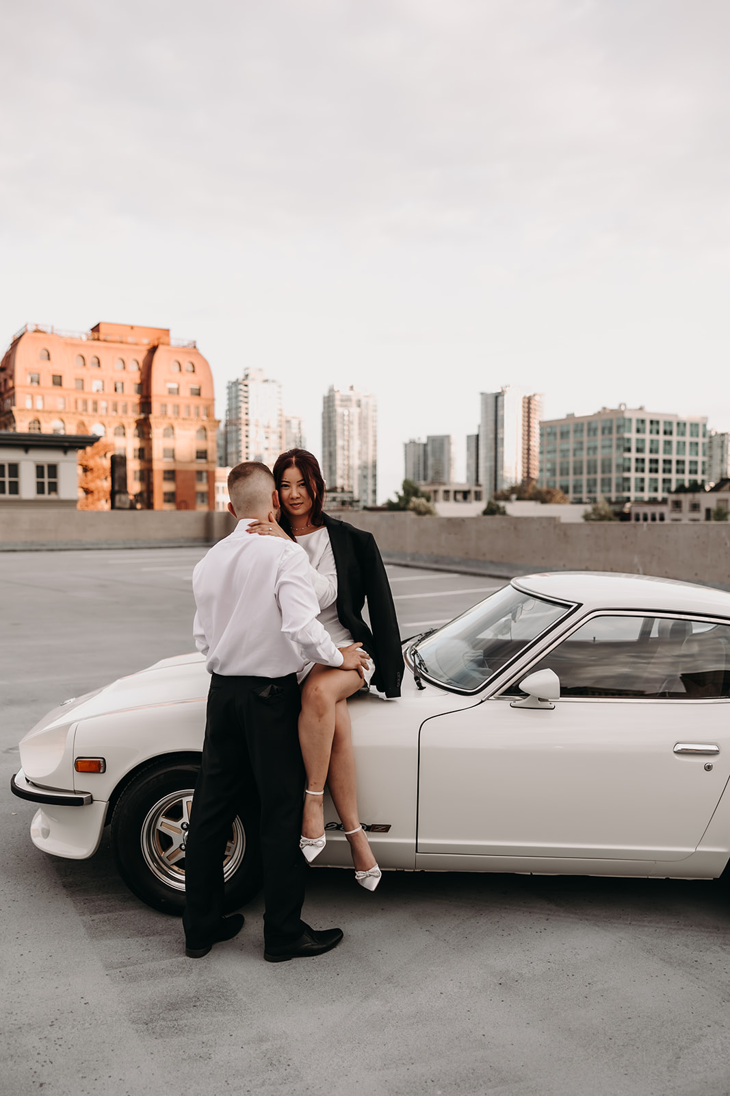 Couple sharing a fun, intimate moment during their city engagement photoshoot in Downtown Vancouver, with the vintage car and city buildings in the background.