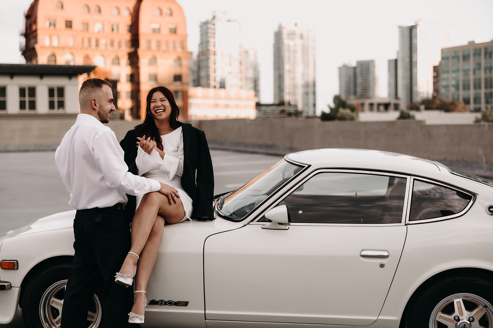 Couple sharing a joyful moment, laughing together during their city engagement photoshoot on a Vancouver rooftop, with stunning city views in the background.