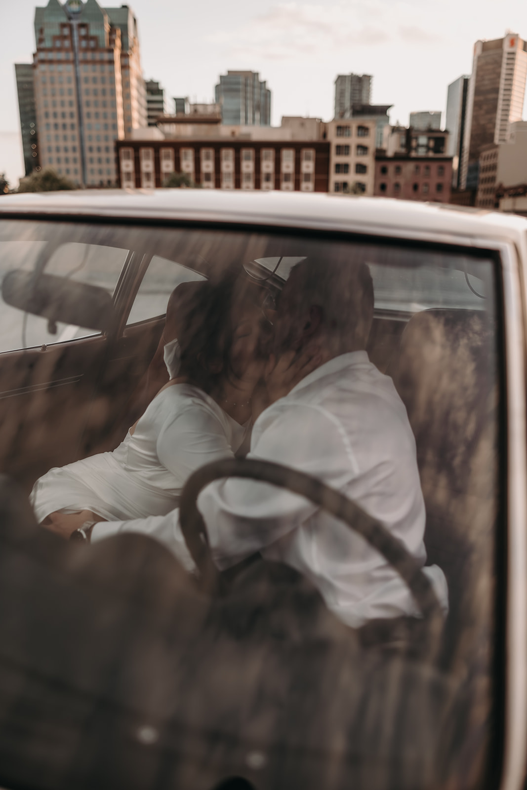 A romantic moment captured during city engagement photos with the couple cuddling in the back seat of a car against the urban backdrop.