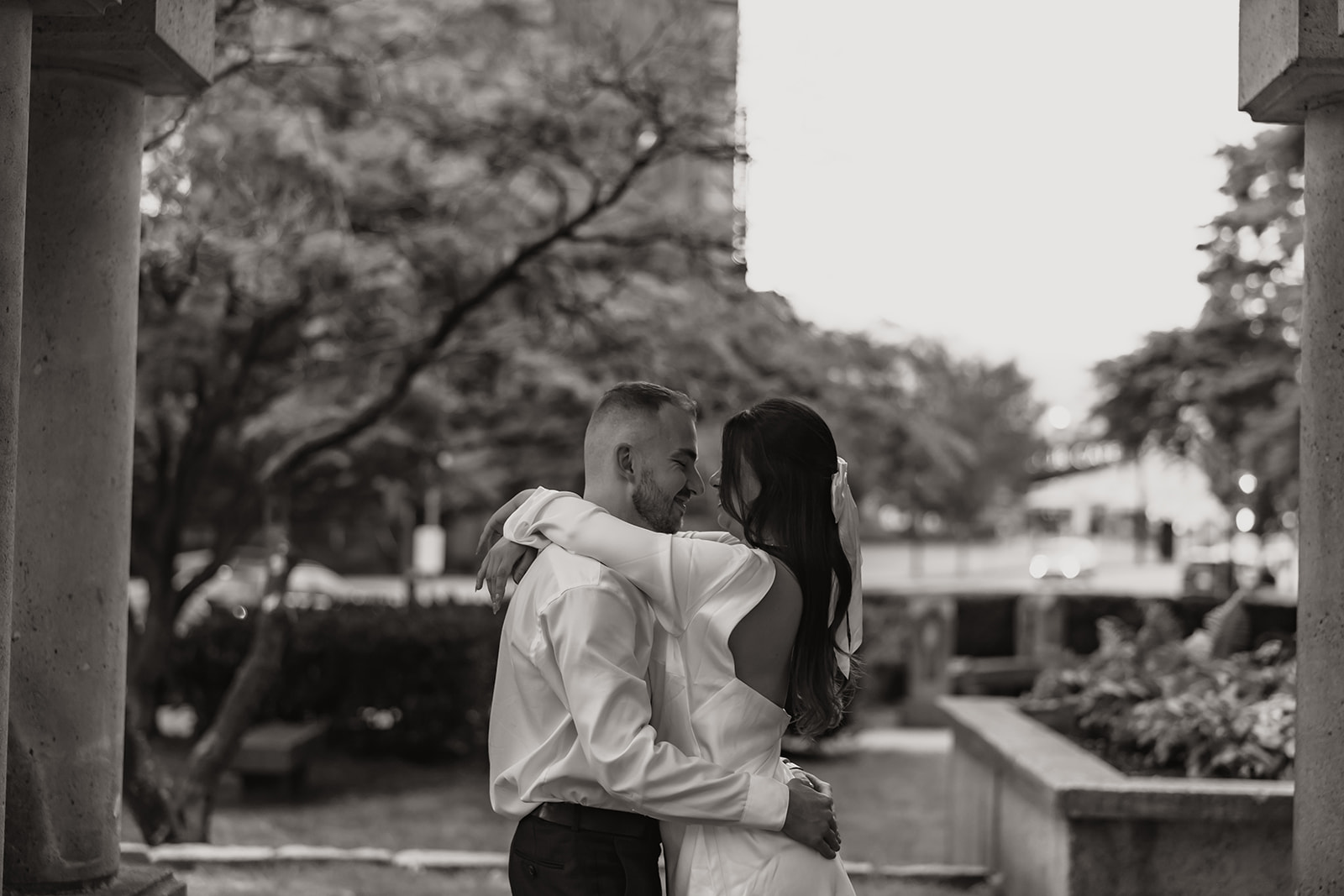 Couple embracing in a city park during their engagement photo shoot, showing genuine happiness.