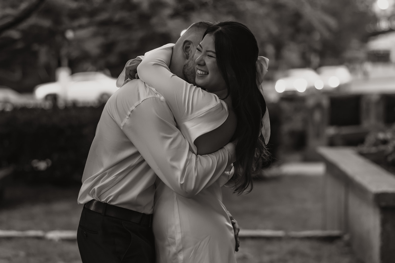 Couple embracing in a city park during their engagement photo shoot, showing genuine happiness.