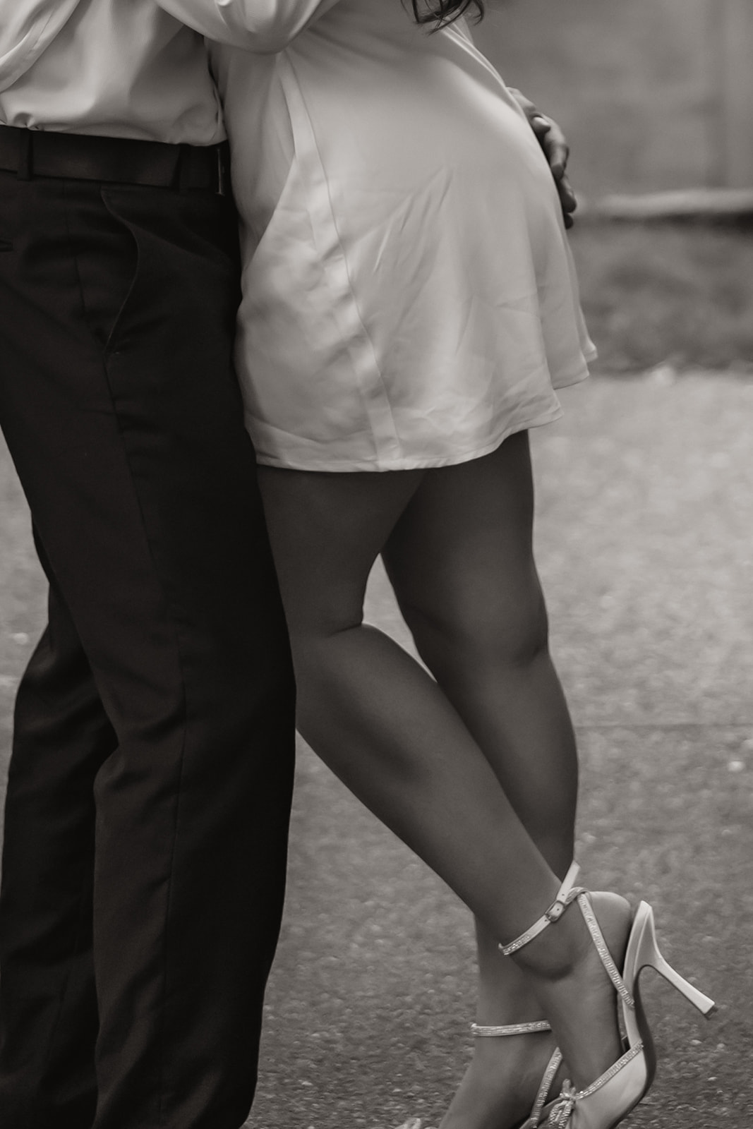 Close-up of the couple's legs intertwined as they embrace in the park, with the woman in white heels.