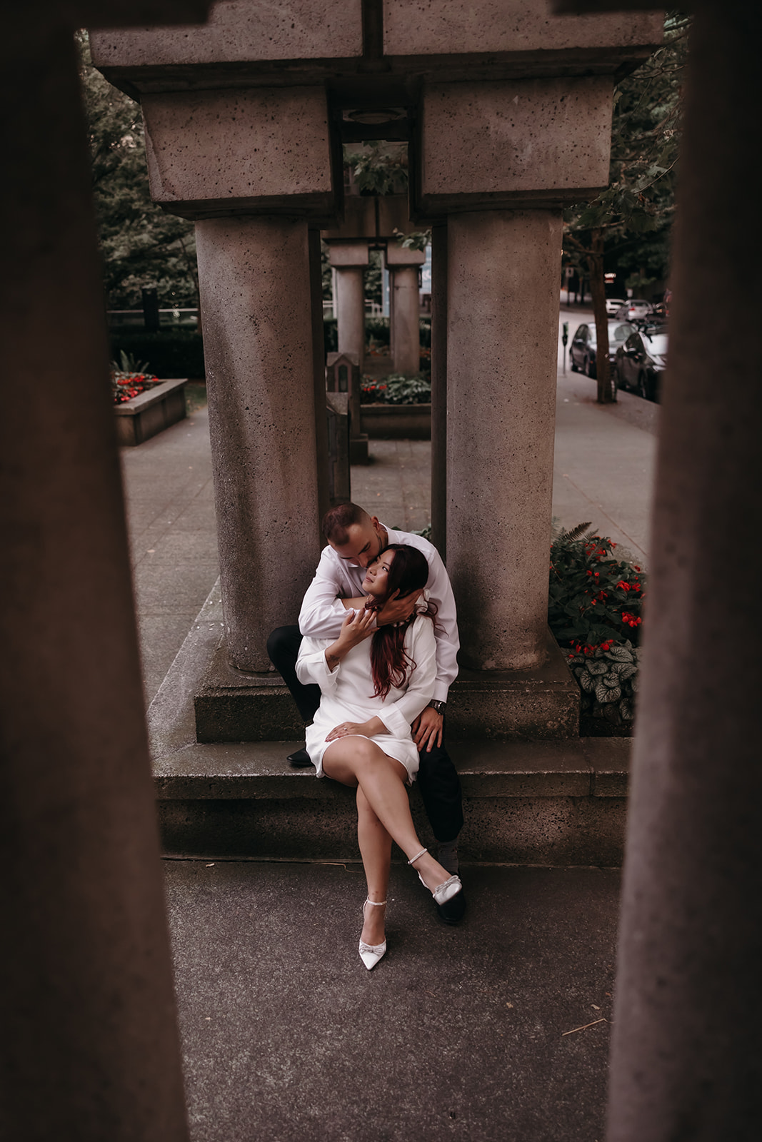 Couple sitting on a stone bench under columns in an urban park, sharing a tender moment.