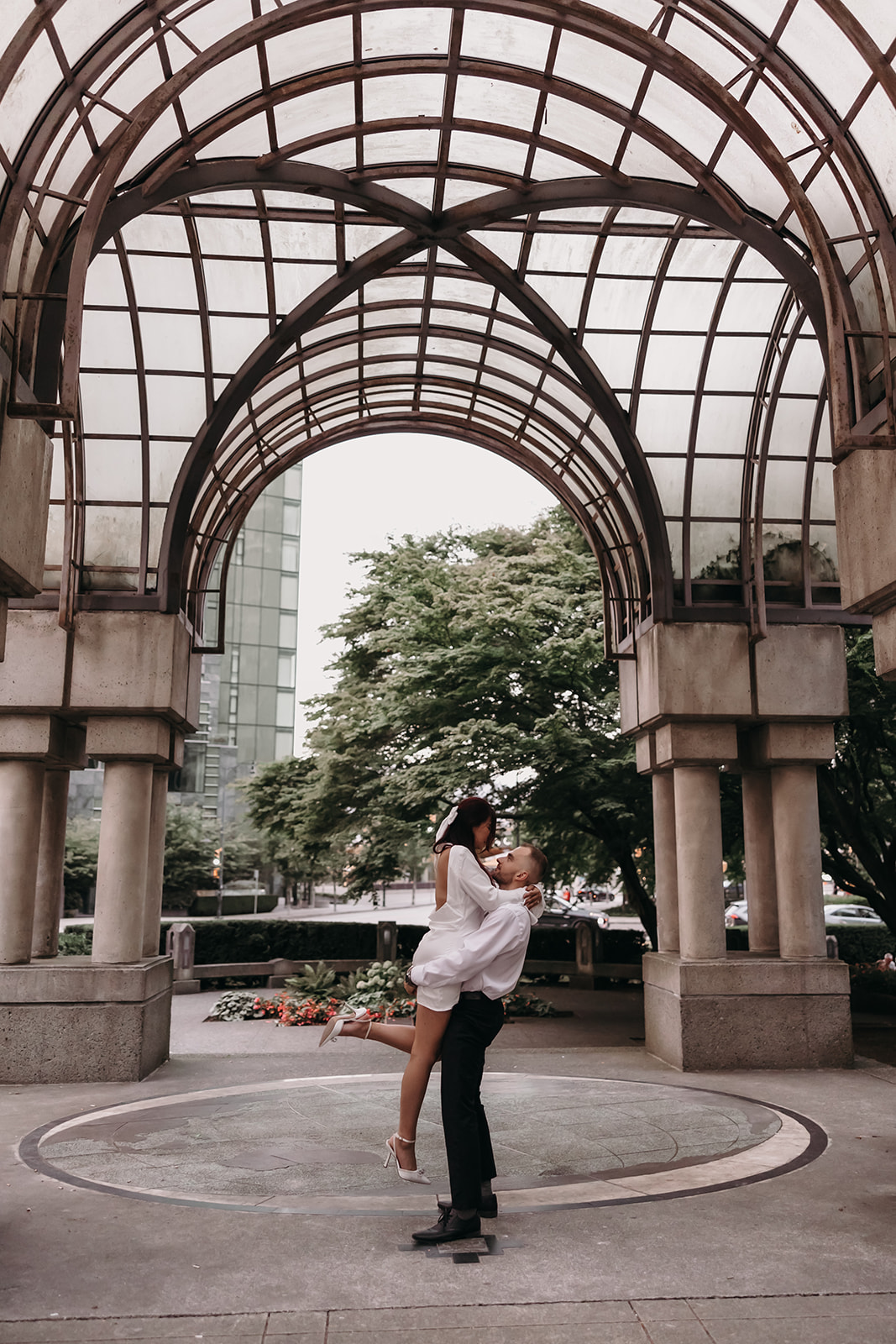 Couple in a city engagement photo, where the man lifts the woman into a romantic pose under a city canopy.