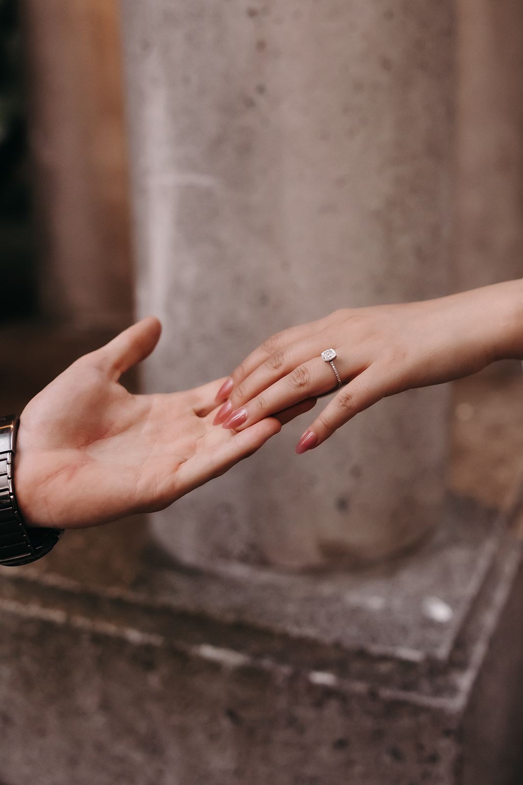 Close-up of an engagement ring as the couple holds hands in a city park, symbolizing their love.