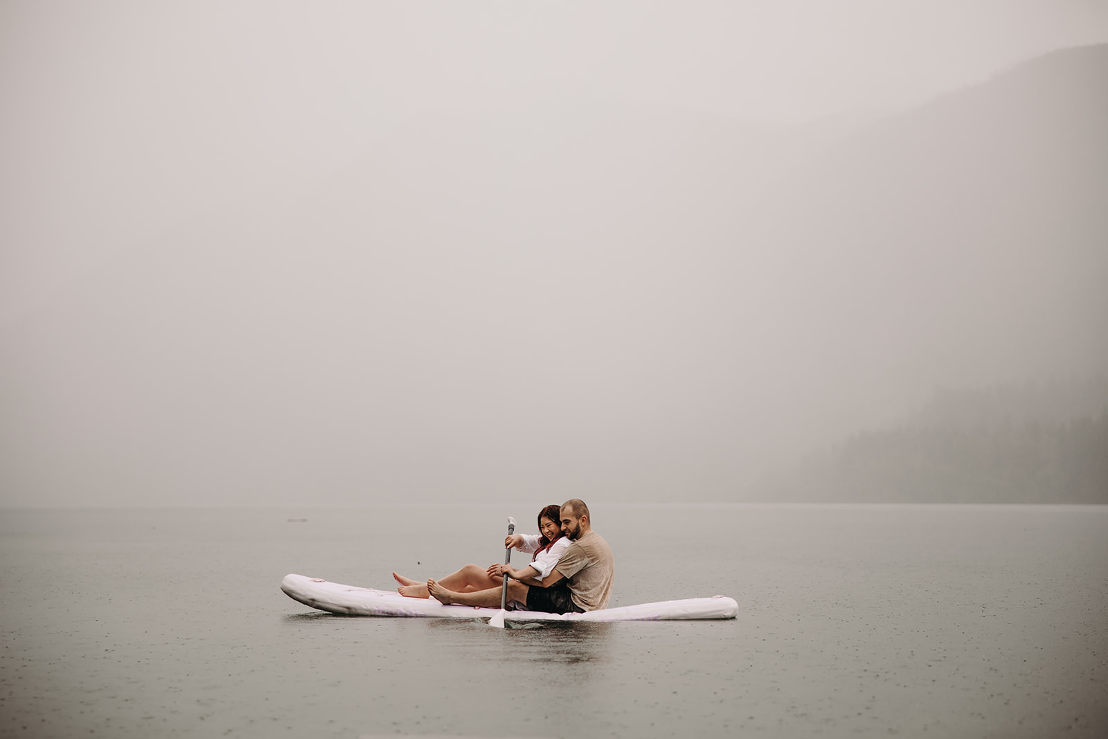 Engaged couple embracing on a paddle board under the rain at Golden Ears Provincial Park.