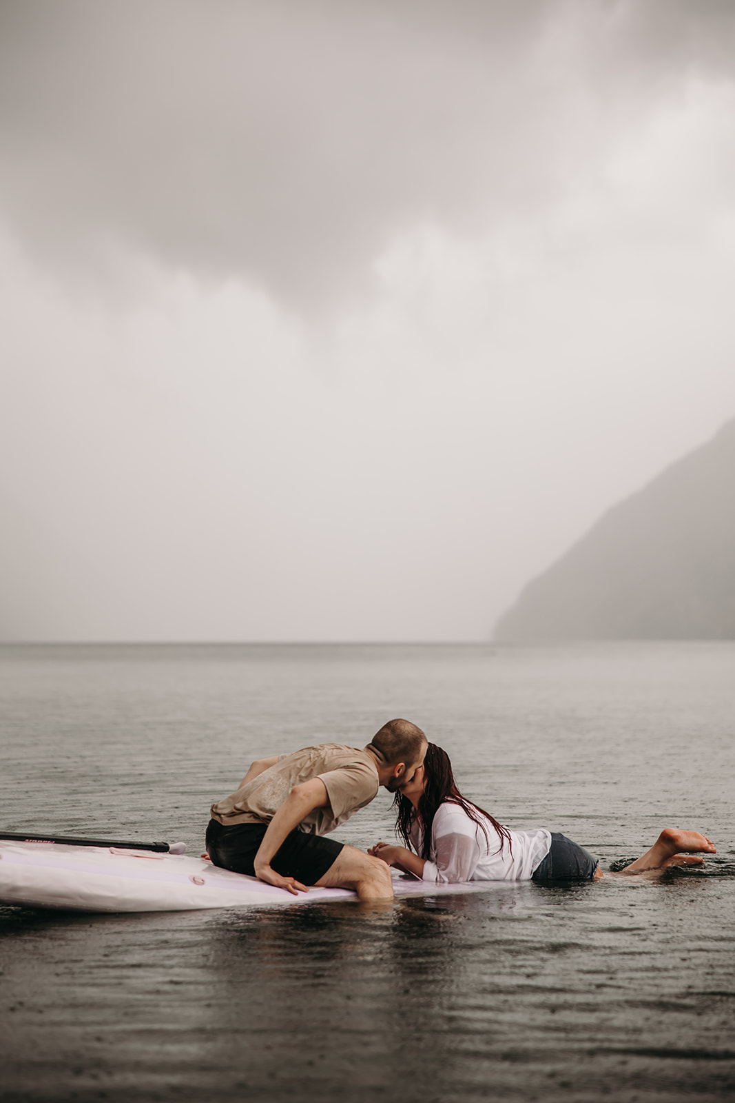 Engaged couple sharing a kiss while sitting on a paddle board in the rain during their BC engagement session.