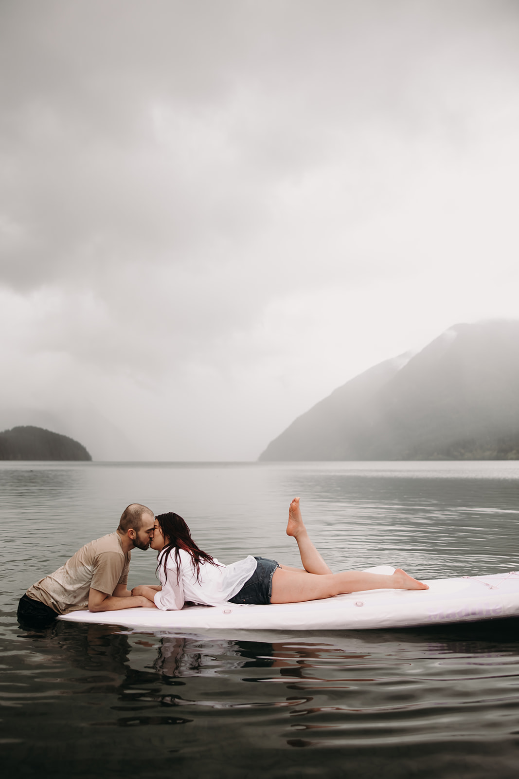 Engaged couple sharing a kiss while sitting on a paddle board in the rain during their BC engagement session.