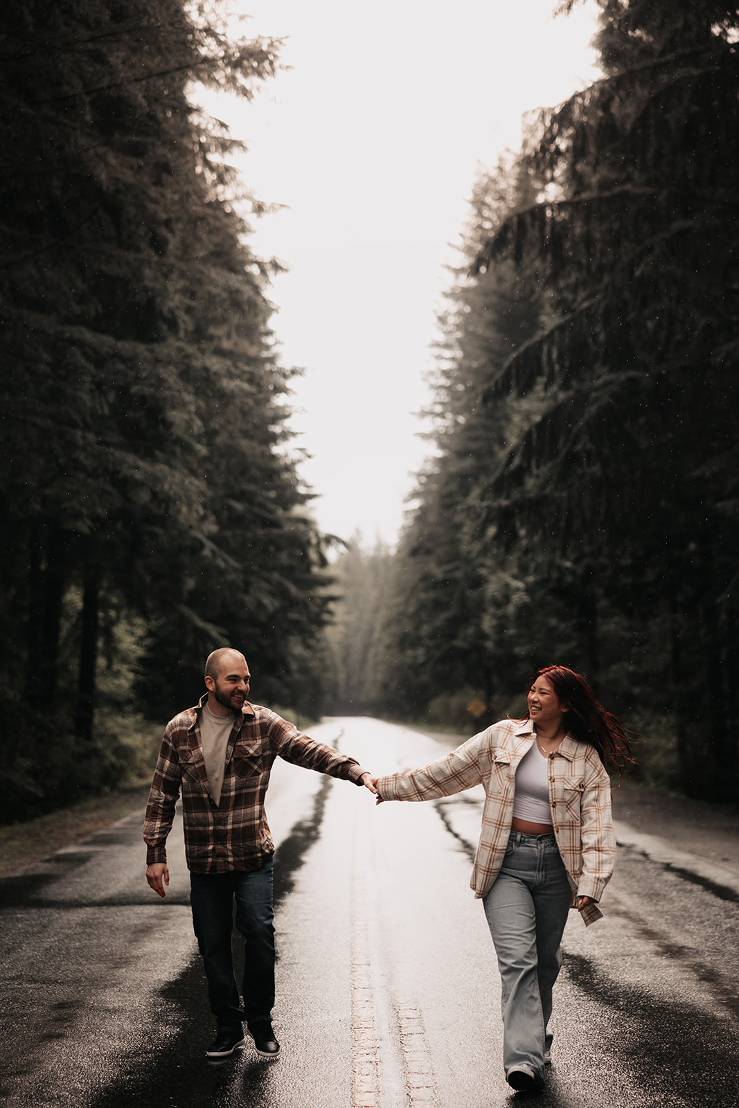 Couple holding hands and walking down a rain-soaked road in Golden Ears Provincial Park during their engagement photoshoot.