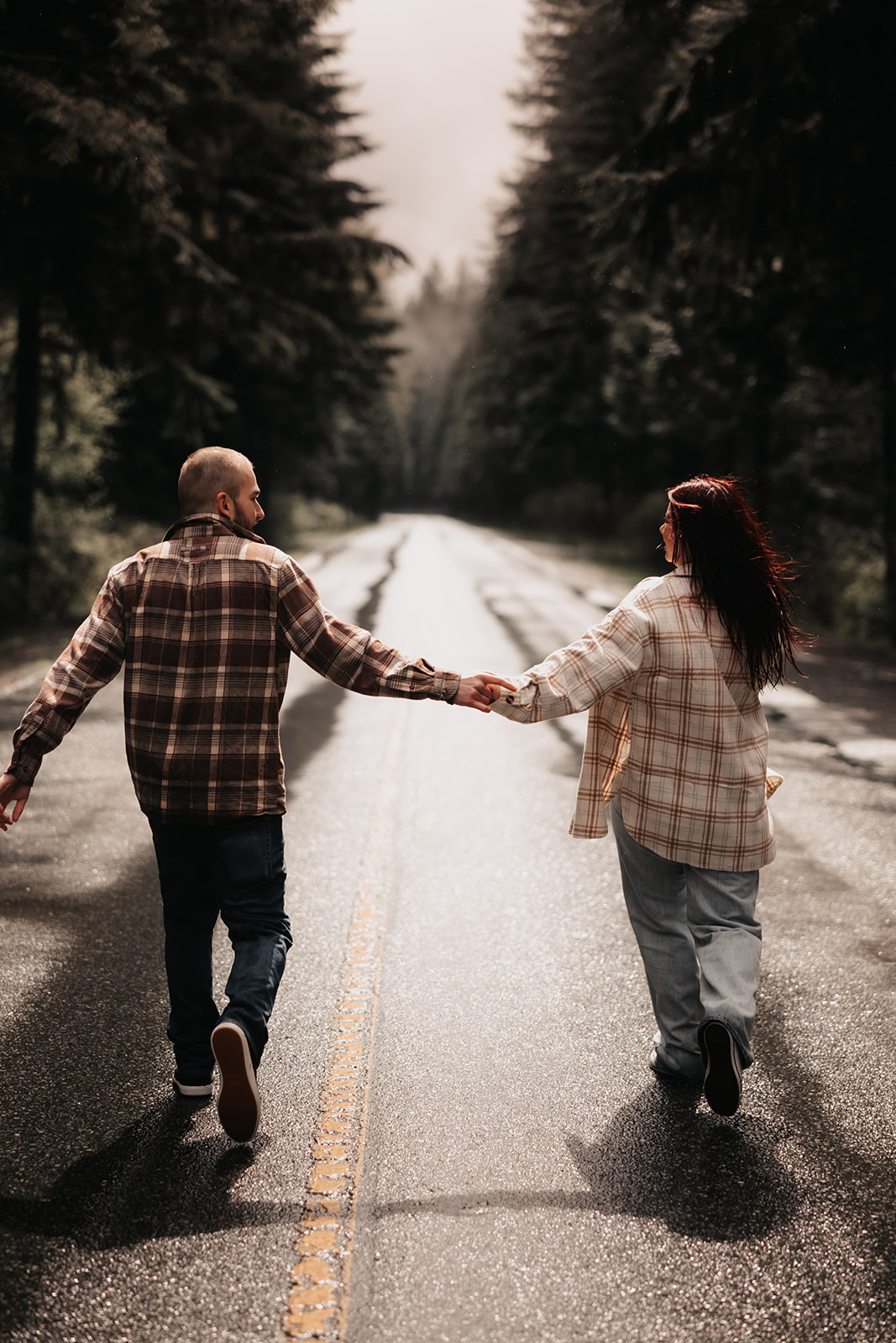 Couple holding hands and walking down a rain-soaked road in Golden Ears Provincial Park during their engagement photoshoot.