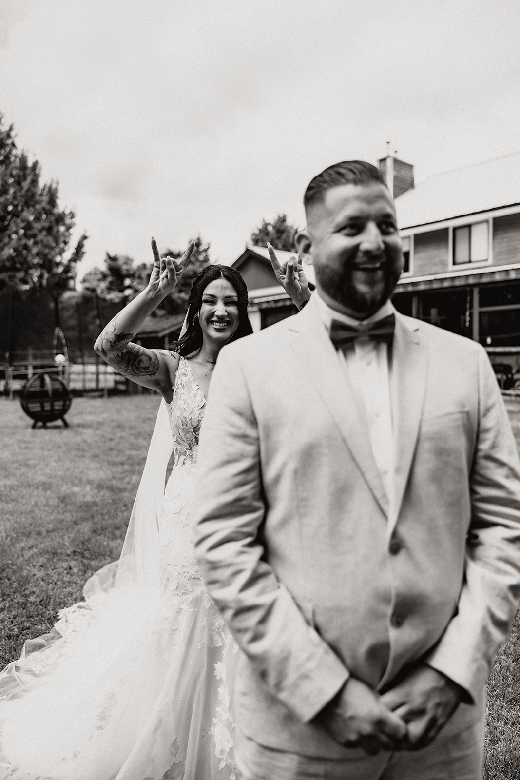 Bride sneaks up behind her groom, making a fun gesture as they prepare for their first look, capturing the moment of lighthearted joy.