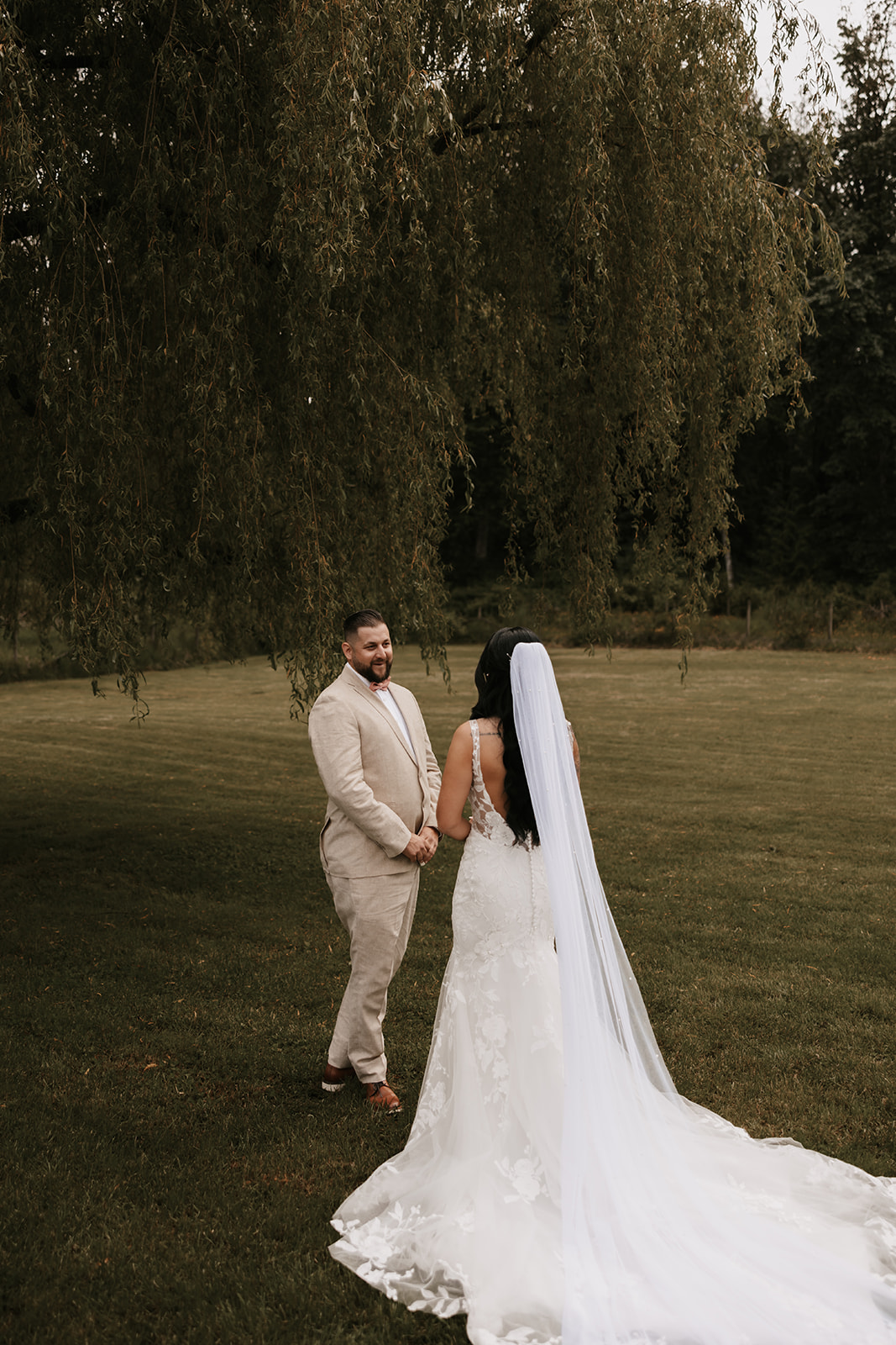 A bride and groom standing together outdoors, with the groom lovingly gazing at the bride as she faces him. The backdrop of nature creates a serene moment between the couple, reminding us of how to enjoy your wedding day by embracing the quiet, intimate moments.