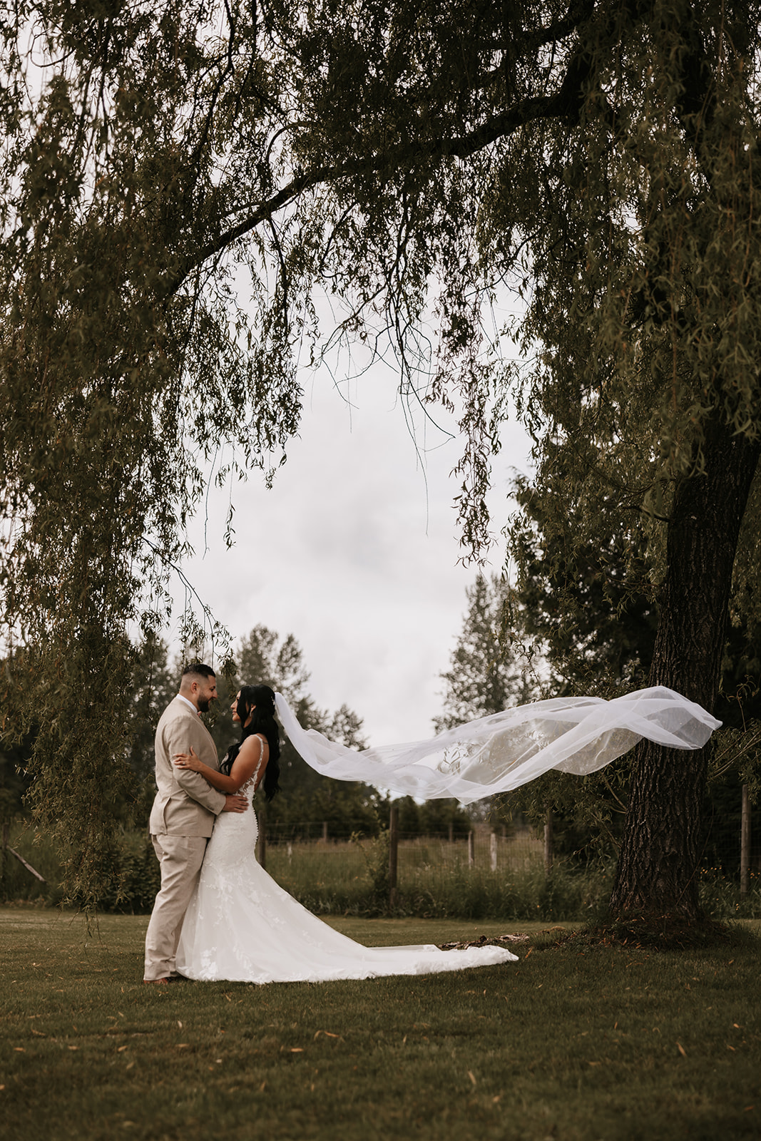 A bride and groom standing together outdoors, with the groom lovingly gazing at the bride as she faces him. The backdrop of nature creates a serene moment between the couple, reminding us of how to enjoy your wedding day by embracing the quiet, intimate moments.