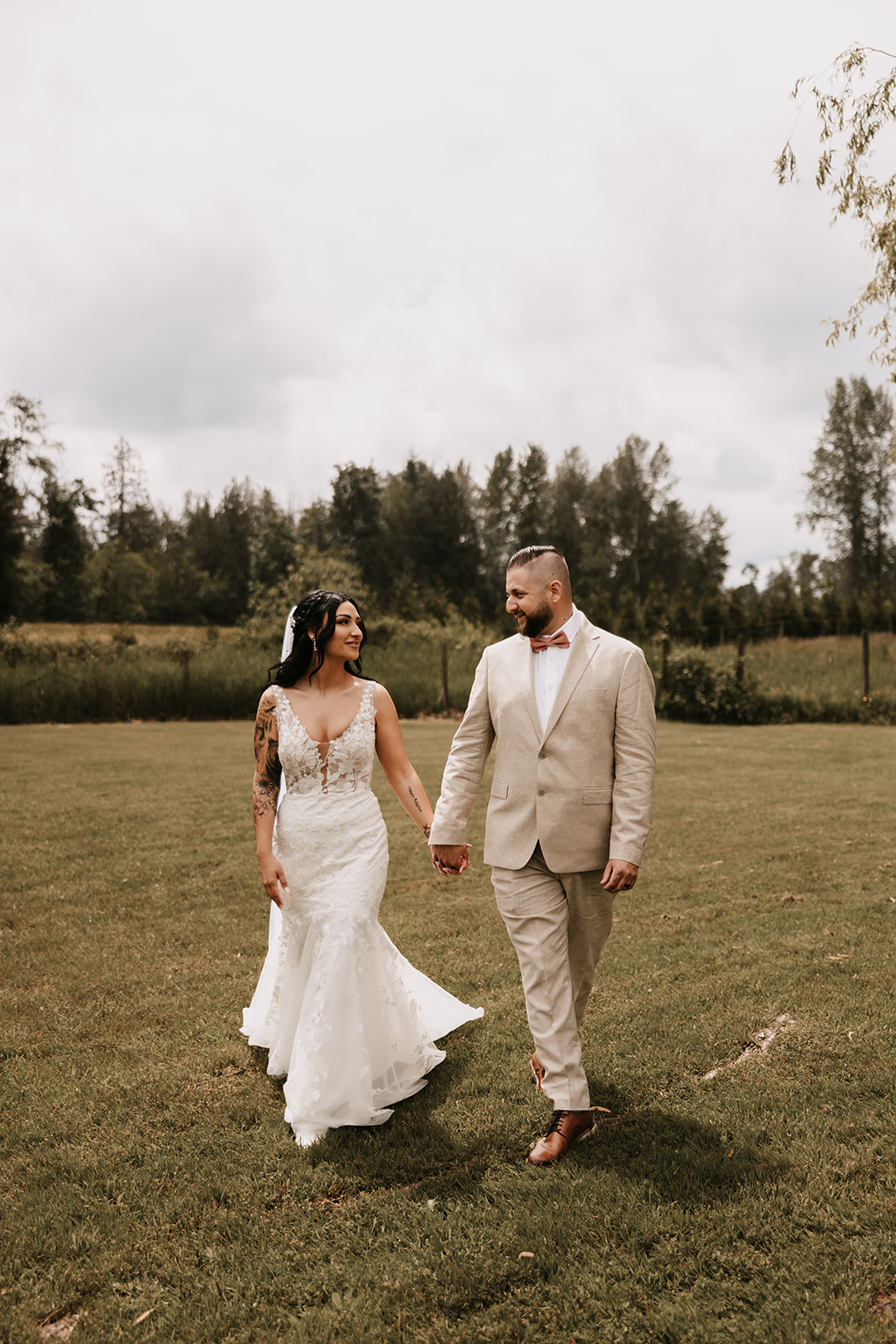 Bride and groom walking outside in a field of grass smiling at eachother