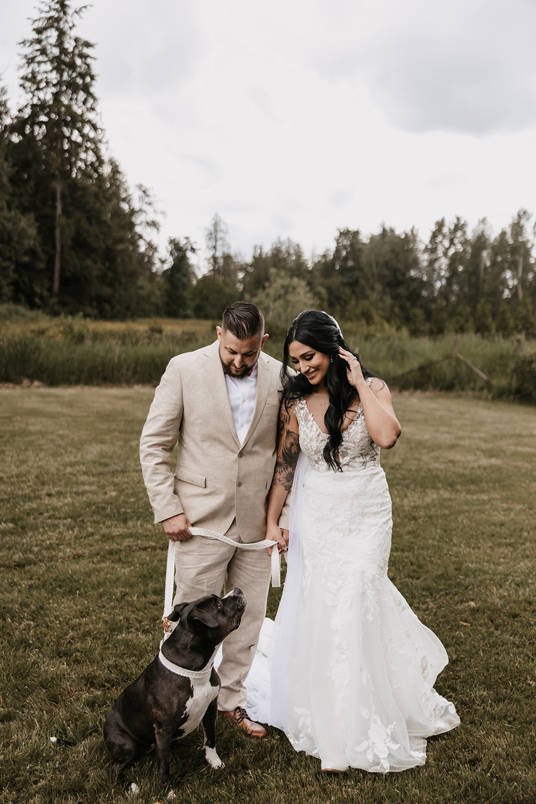 Bride and groom smiling at their dog during wedding portraits, making memories with their furry companion as they enjoy every moment of their special day.