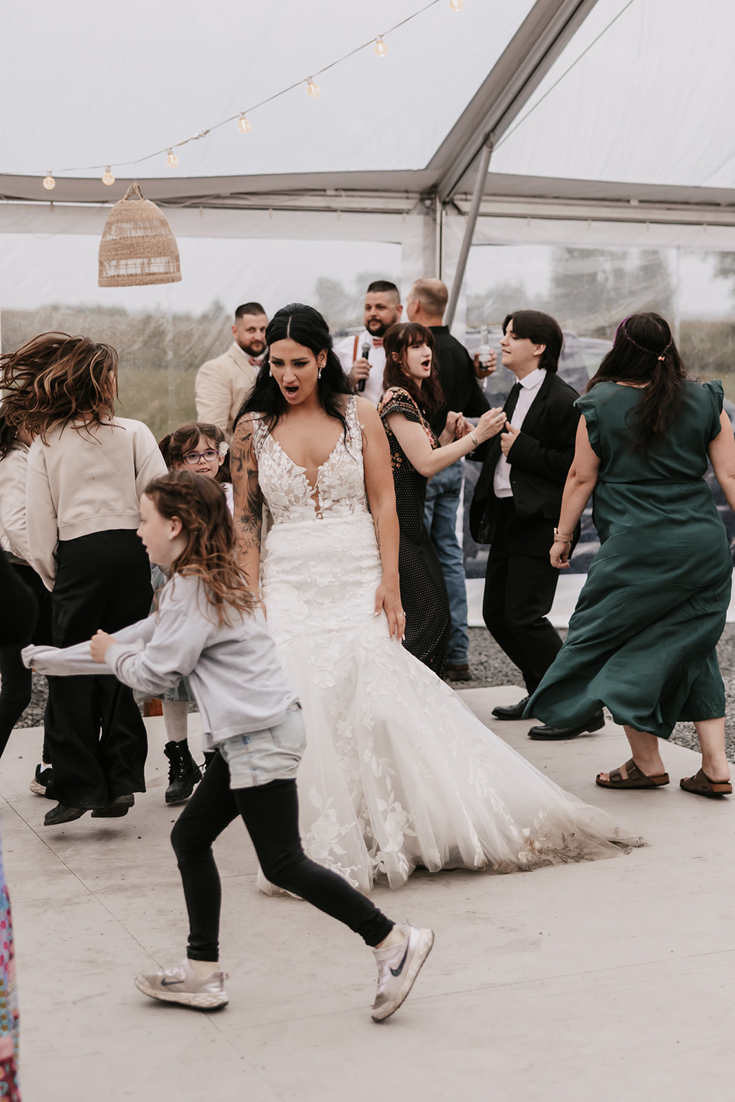 A lively wedding reception scene under a tent with guests dancing. The bride is at the center, enjoying the moment as she dances with a joyful expression. A reminder of how to enjoy your wedding day by fully embracing the celebration.