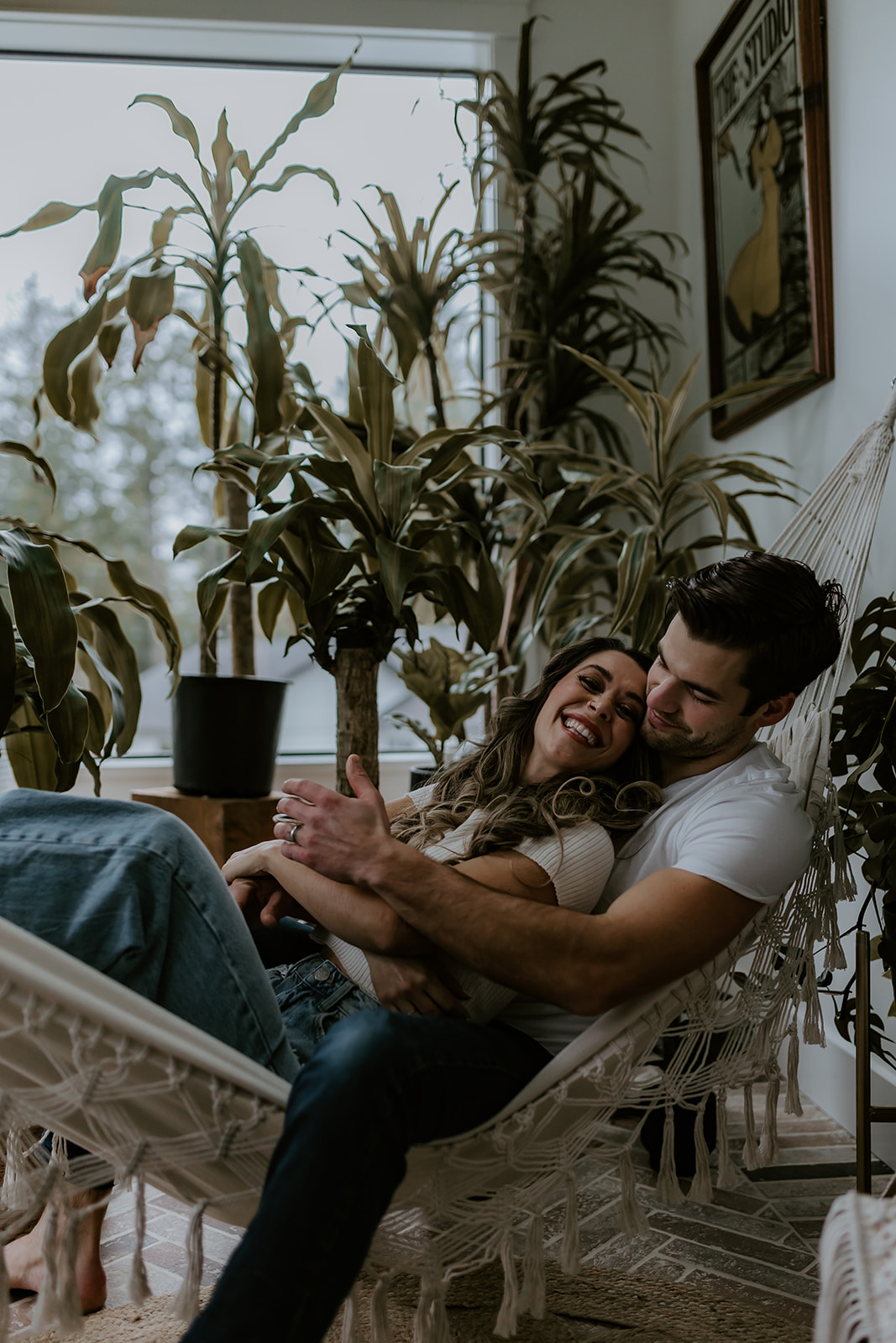 A couple sharing a loving moment in a hammock surrounded by lush plants, laughing and enjoying each other's company, demonstrating relaxed and fun engagement photo ideas.