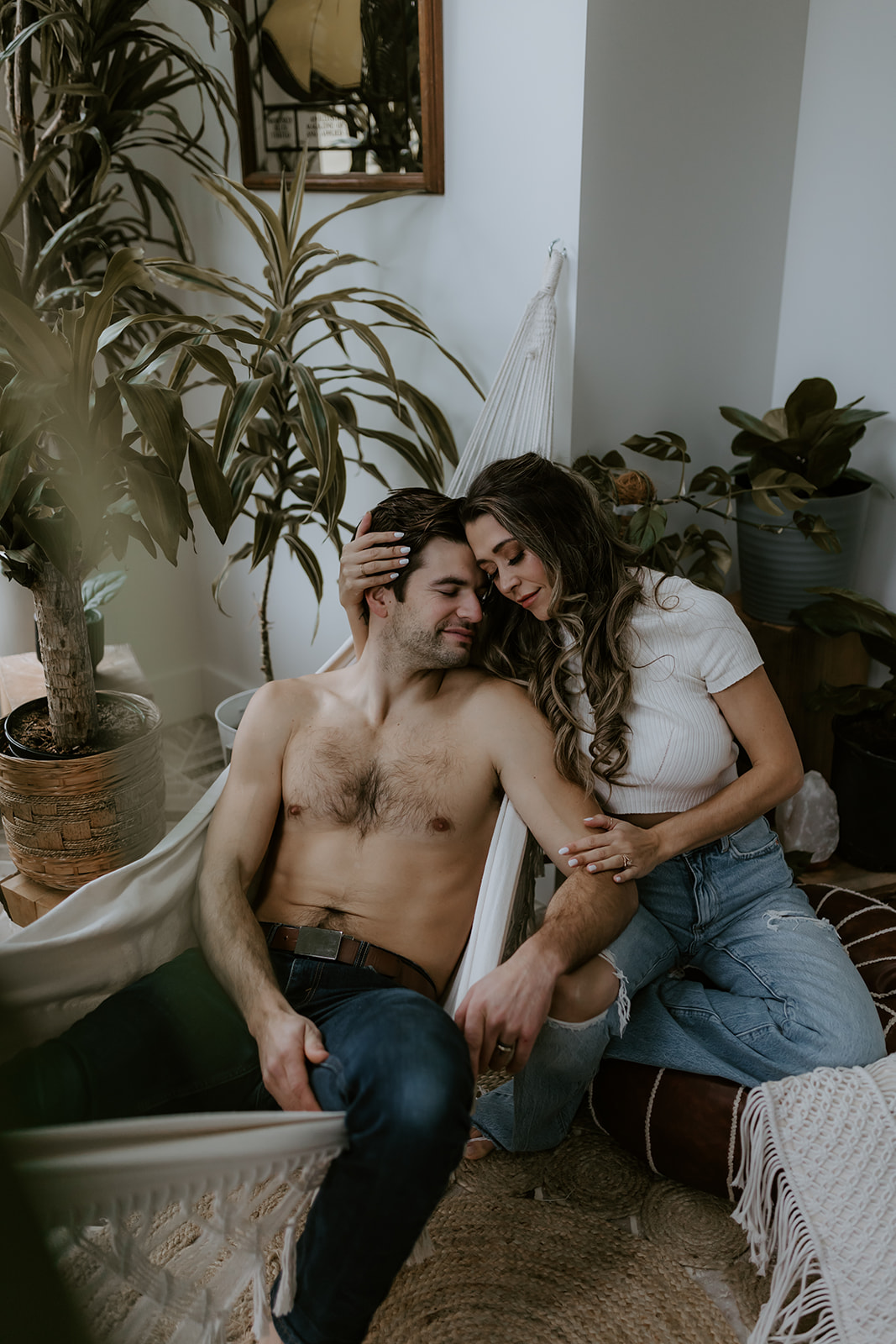 A couple embracing and snuggling in a hammock surrounded by plants, showcasing intimate moments perfect for fun engagement photo ideas.