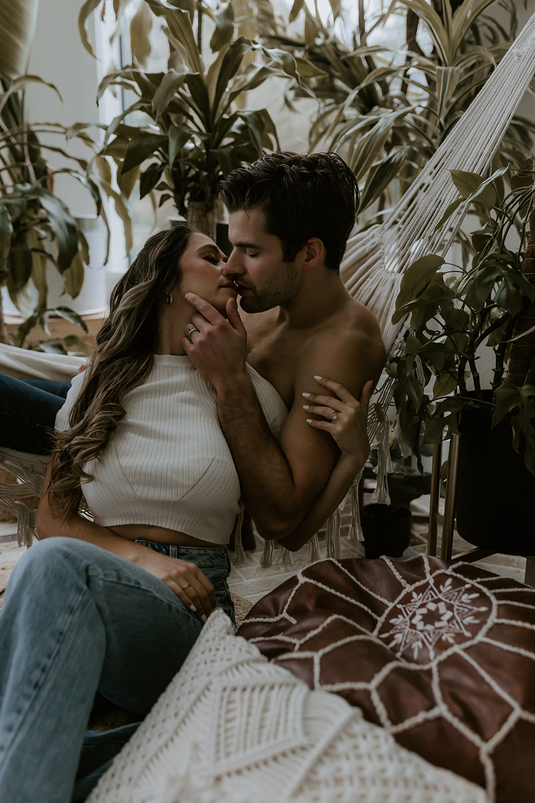 A couple sharing a tender moment in a hammock, enjoying each other's presence in a natural setting full of plants, ideal for cozy and fun engagement photo ideas.