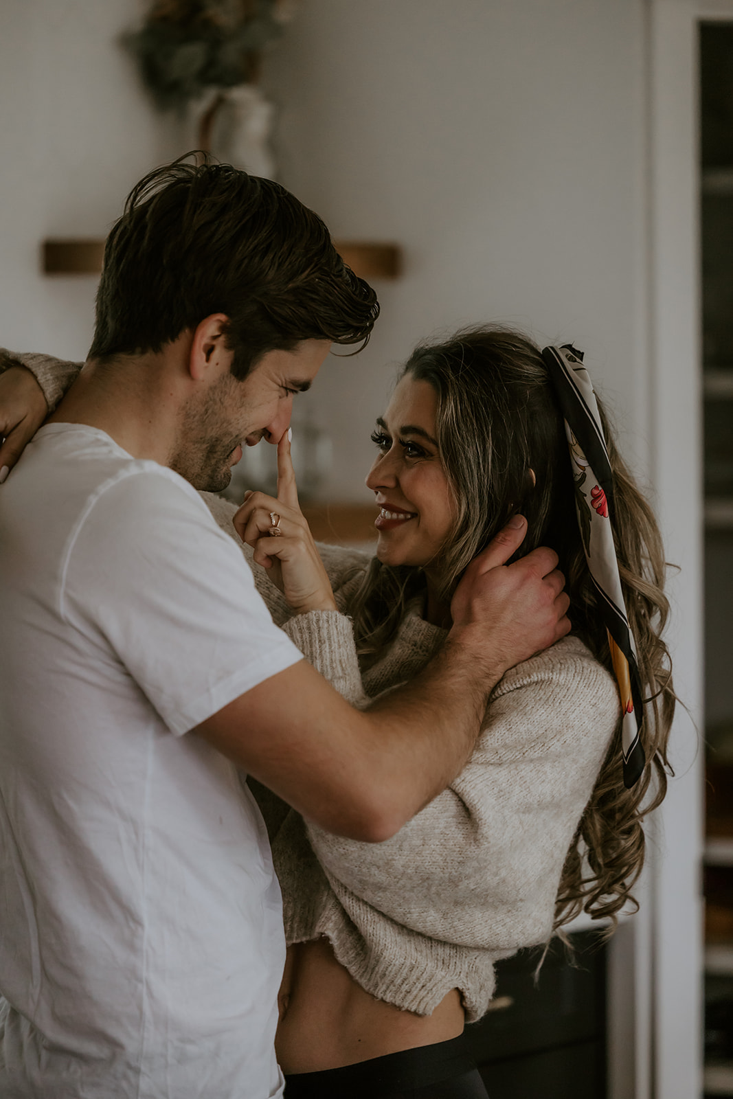 Close-up of a couple in the kitchen sharing a tender moment, with the woman playfully touching the man’s nose, capturing a natural and intimate moment.