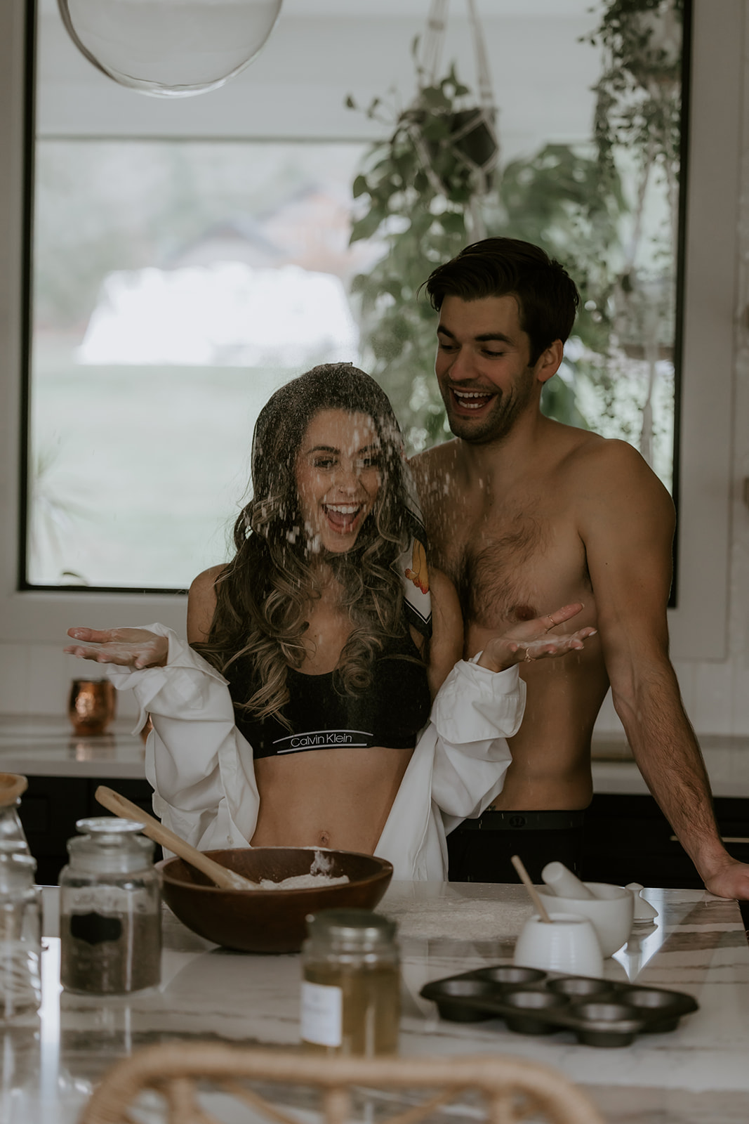 A playful moment in the kitchen where flour is being tossed in the air, with the couple laughing and enjoying their time together, embracing the fun of the engagement shoot.