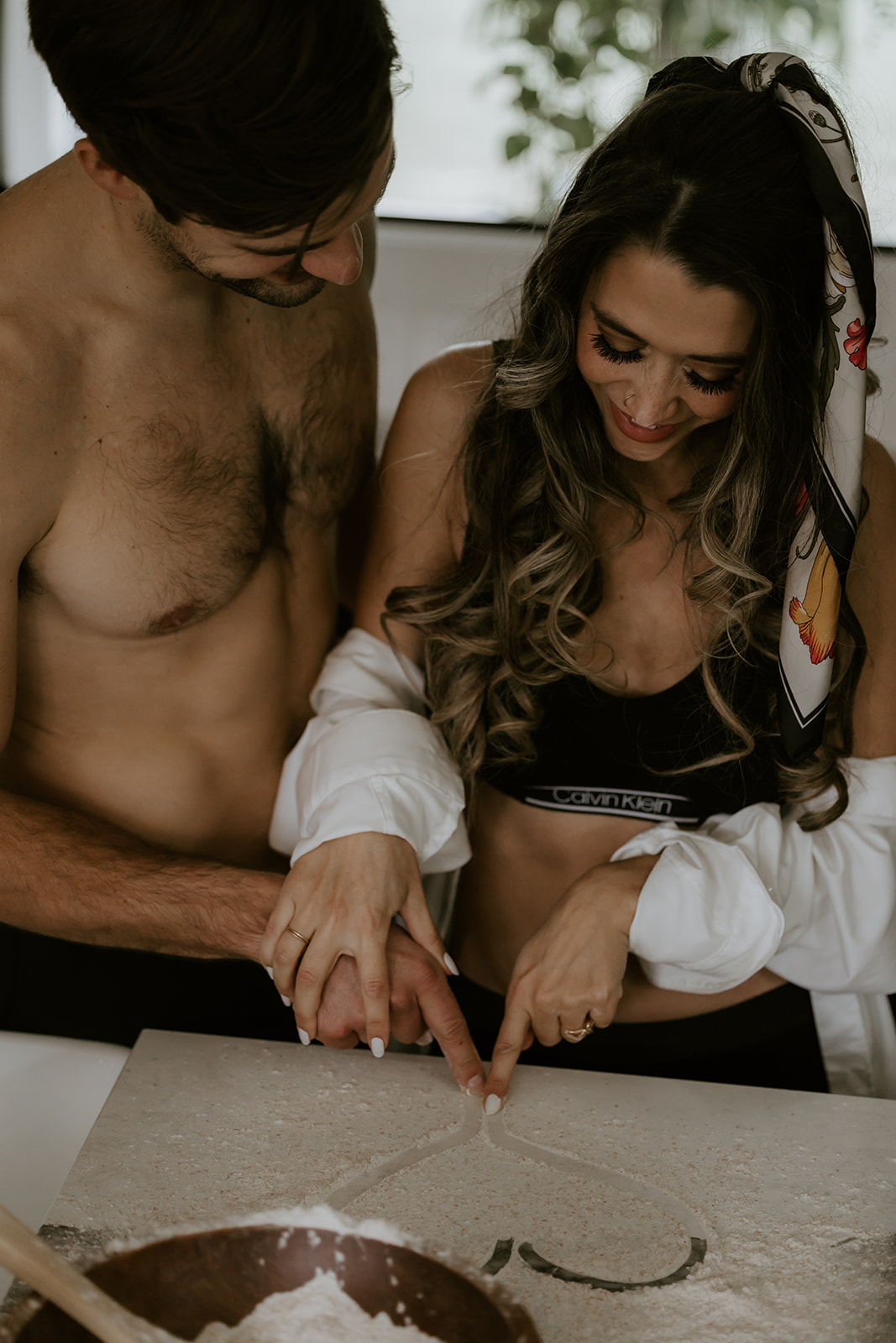 A couple’s hands drawing a heart in flour together while baking in the kitchen, showcasing a sweet and intimate moment during their fun engagement photo ideas session.