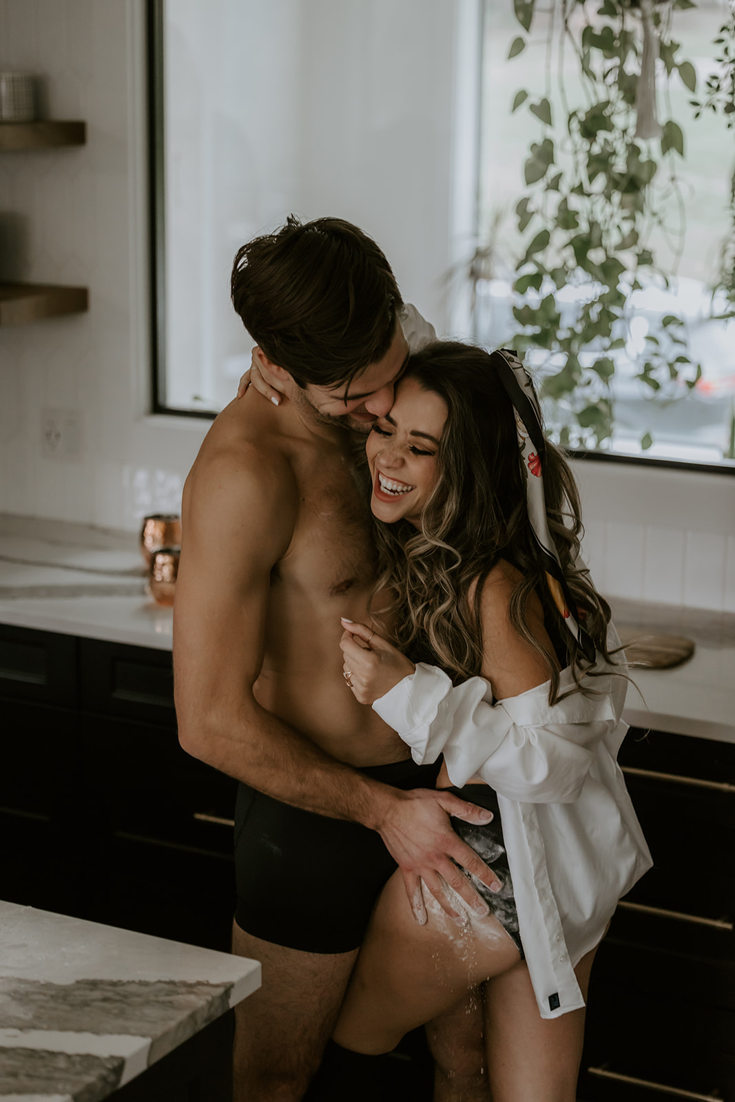 A playful, intimate moment in the kitchen with a couple laughing and enjoying each other’s company as they embrace, creating memories during a fun engagement shoot.