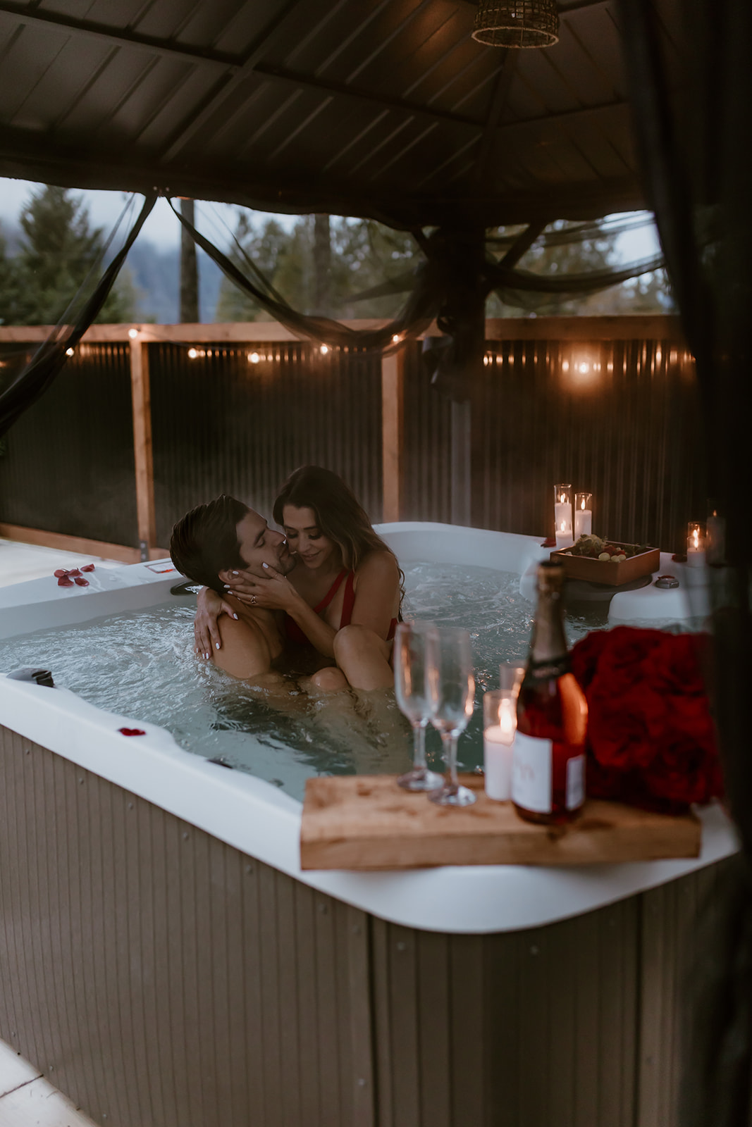 A couple enjoying a bubbly champagne toast in a hot tub, with water splashing around them, adding an element of excitement to their engagement photos.