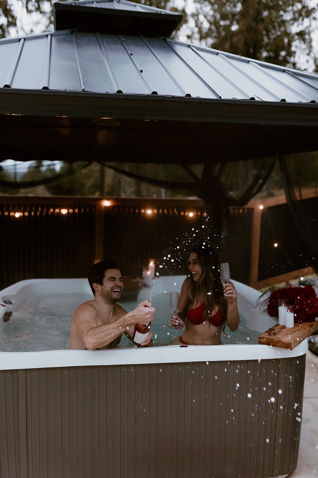 A couple laughing and celebrating in a hot tub, capturing the joy and playfulness of their relationship—perfect for fun engagement photo ideas.