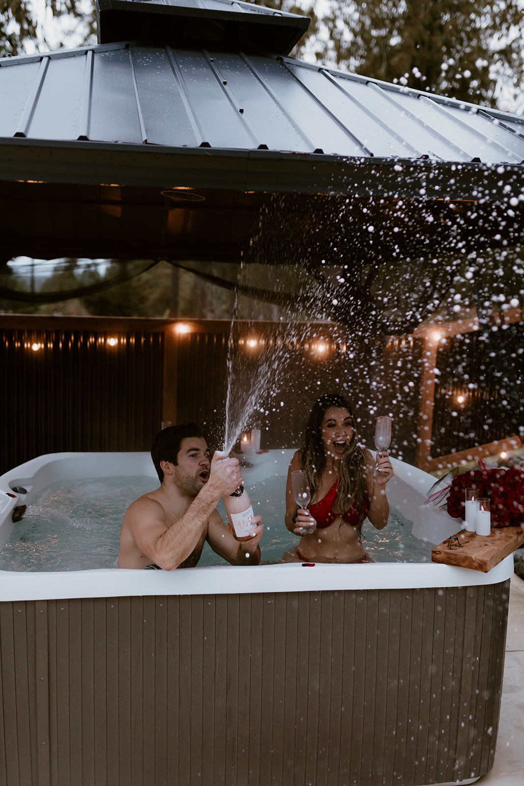 A couple laughing and celebrating in a hot tub, capturing the joy and playfulness of their relationship—perfect for fun engagement photo ideas.