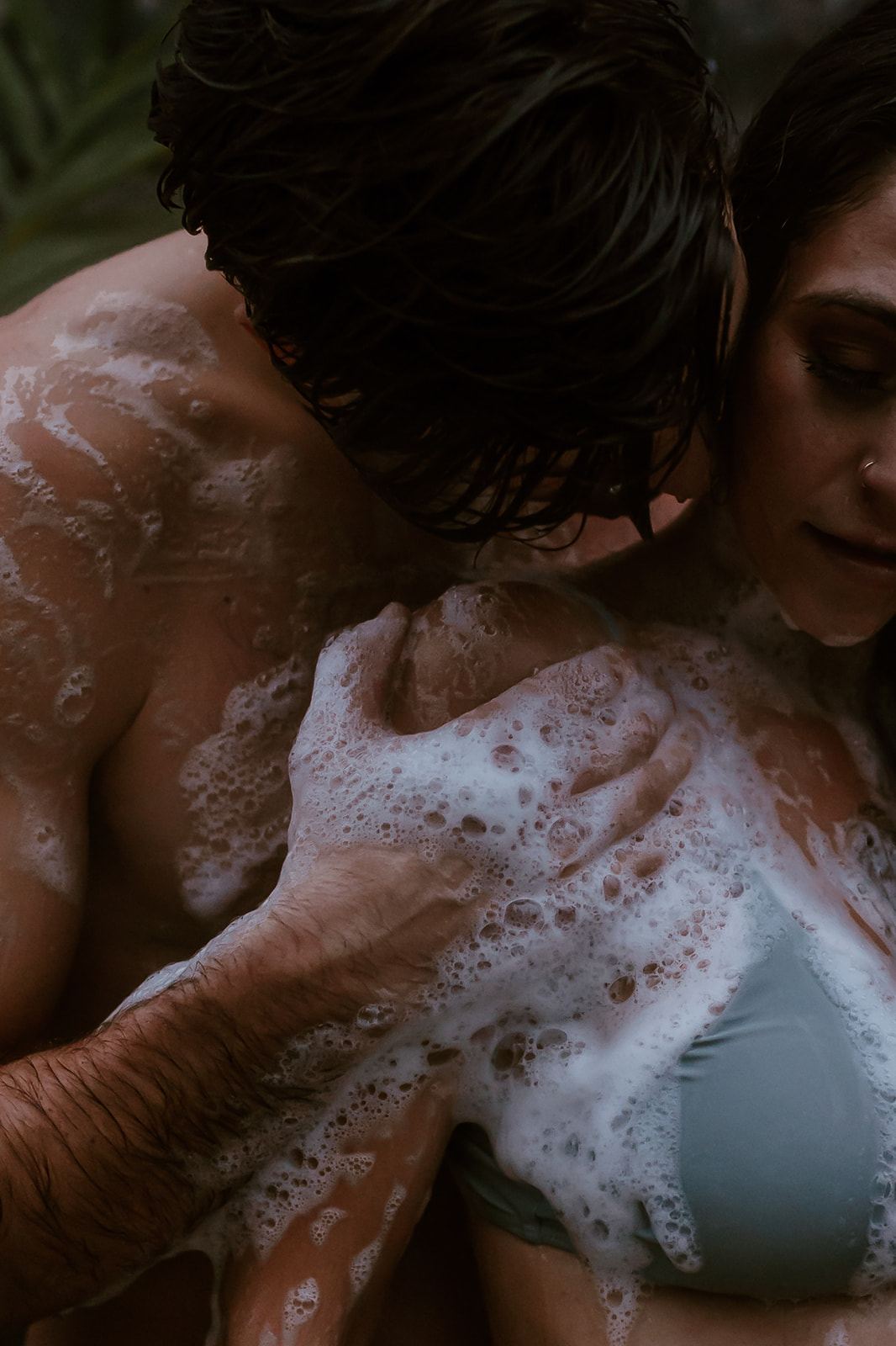 Couple playfully taking an outdoor shower together for their fun engagement photoshoot