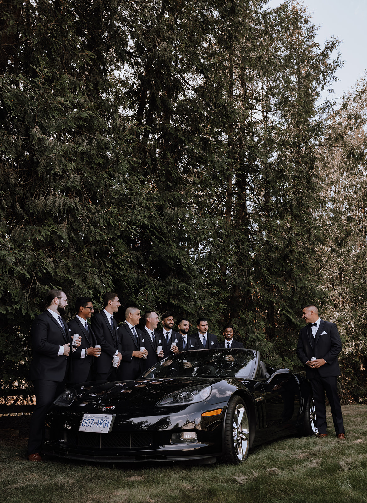 Groomsmen celebrating together near a sleek black convertible before the ceremony at a stylish backyard wedding location.