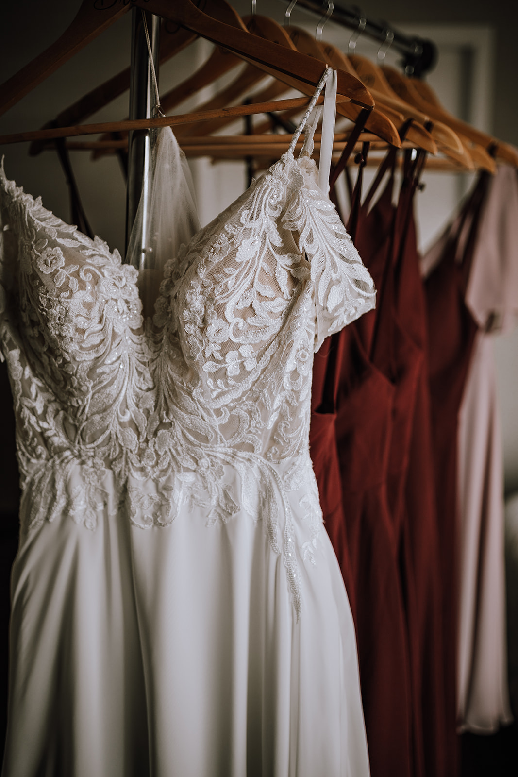 Bridal gown hanging with bridesmaid dresses at a backyard wedding, showcasing the delicate details of the bride's dress alongside the bridesmaids' attire.