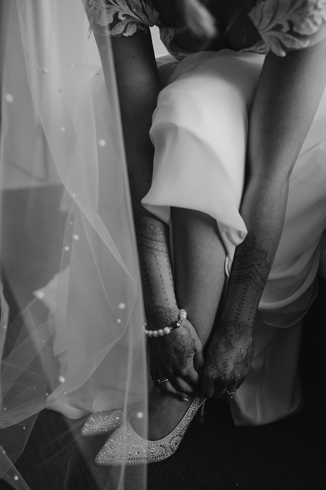 Bride adjusting her sparkling shoes before her backyard wedding ceremony, with her veil and henna-painted hands adding personal touches to the moment.