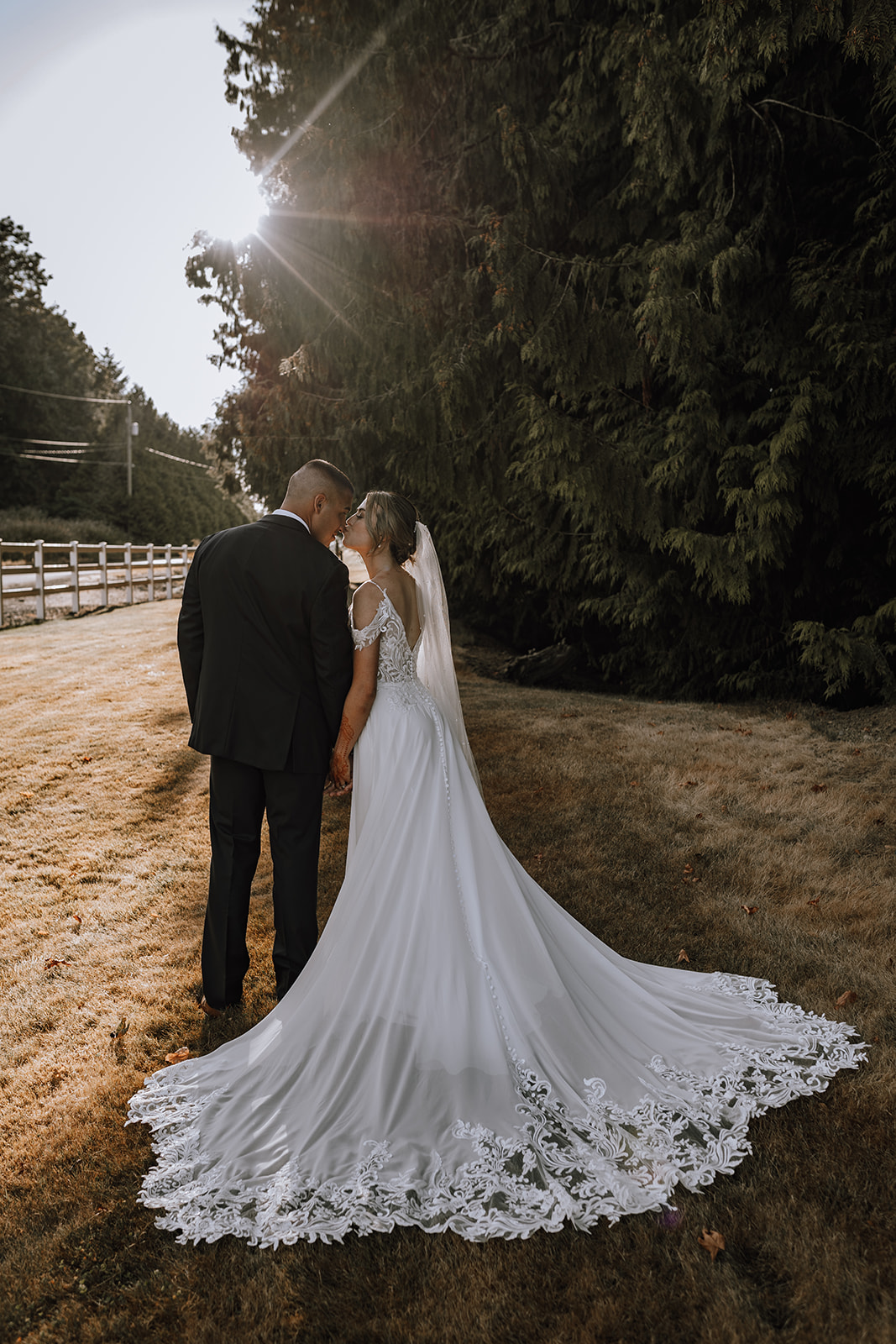 The bride and groom share a quiet moment in their backyard wedding, with the bride's beautiful lace dress flowing as they embrace against a natural backdrop.