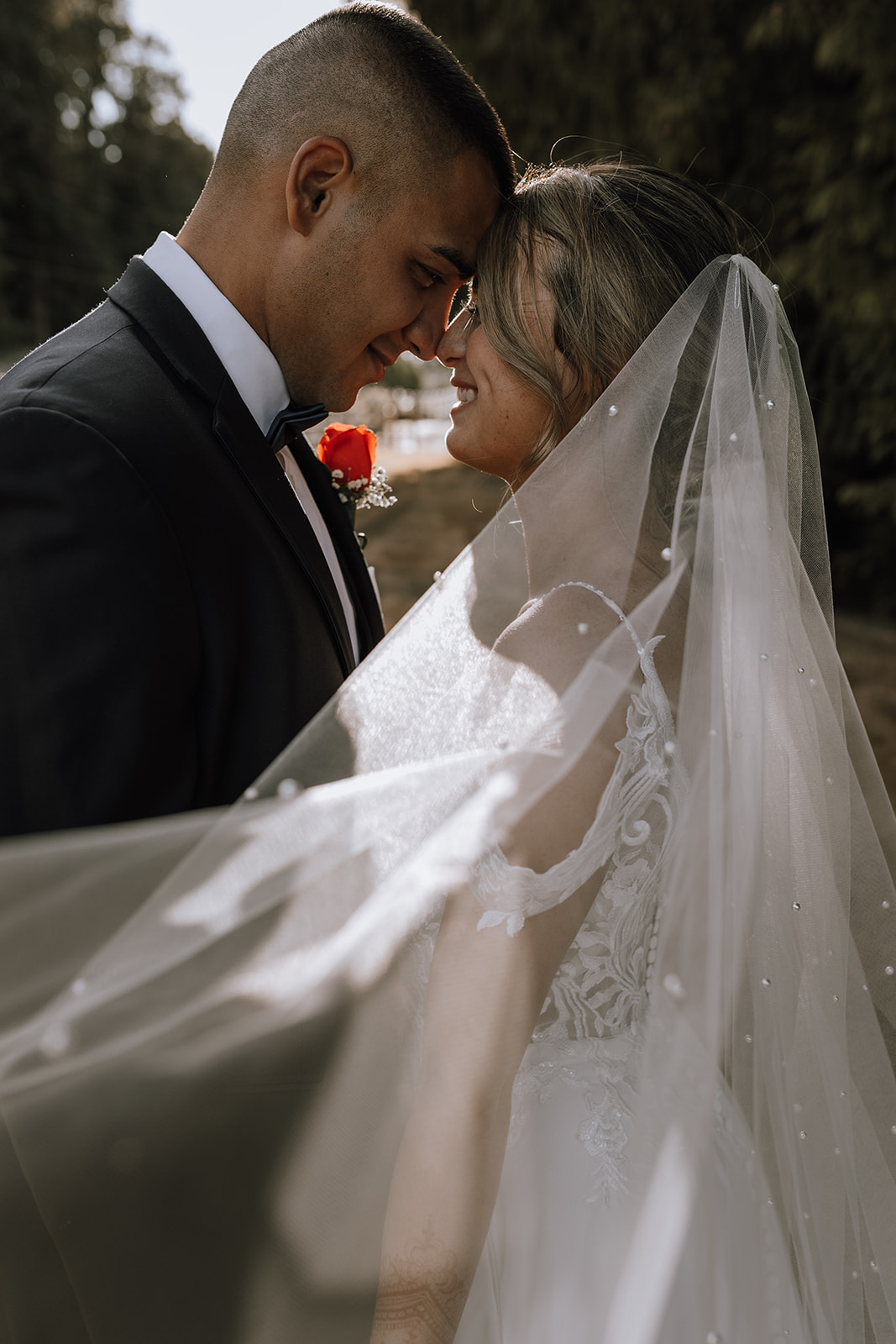 The bride and groom share a quiet moment in their backyard wedding, with the bride's beautiful lace dress flowing as they embrace against a natural backdrop.