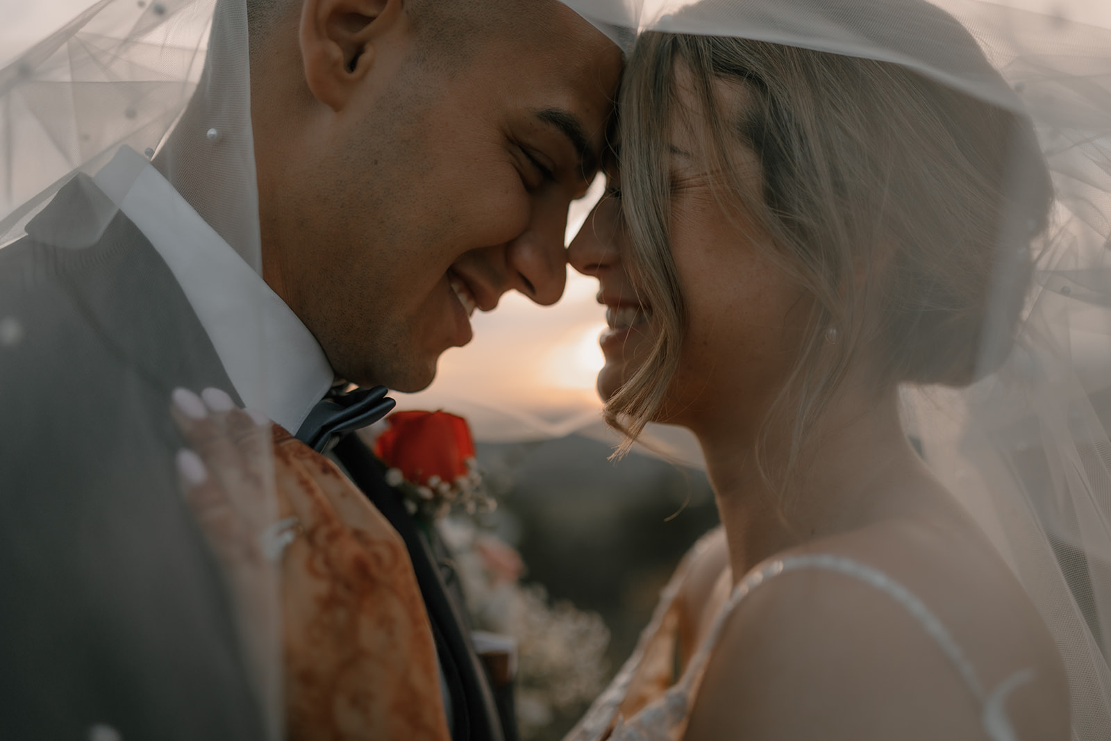 A candid shot of the couple smiling together during their backyard wedding, their love illuminated by the natural light and their vibrant floral bouquet